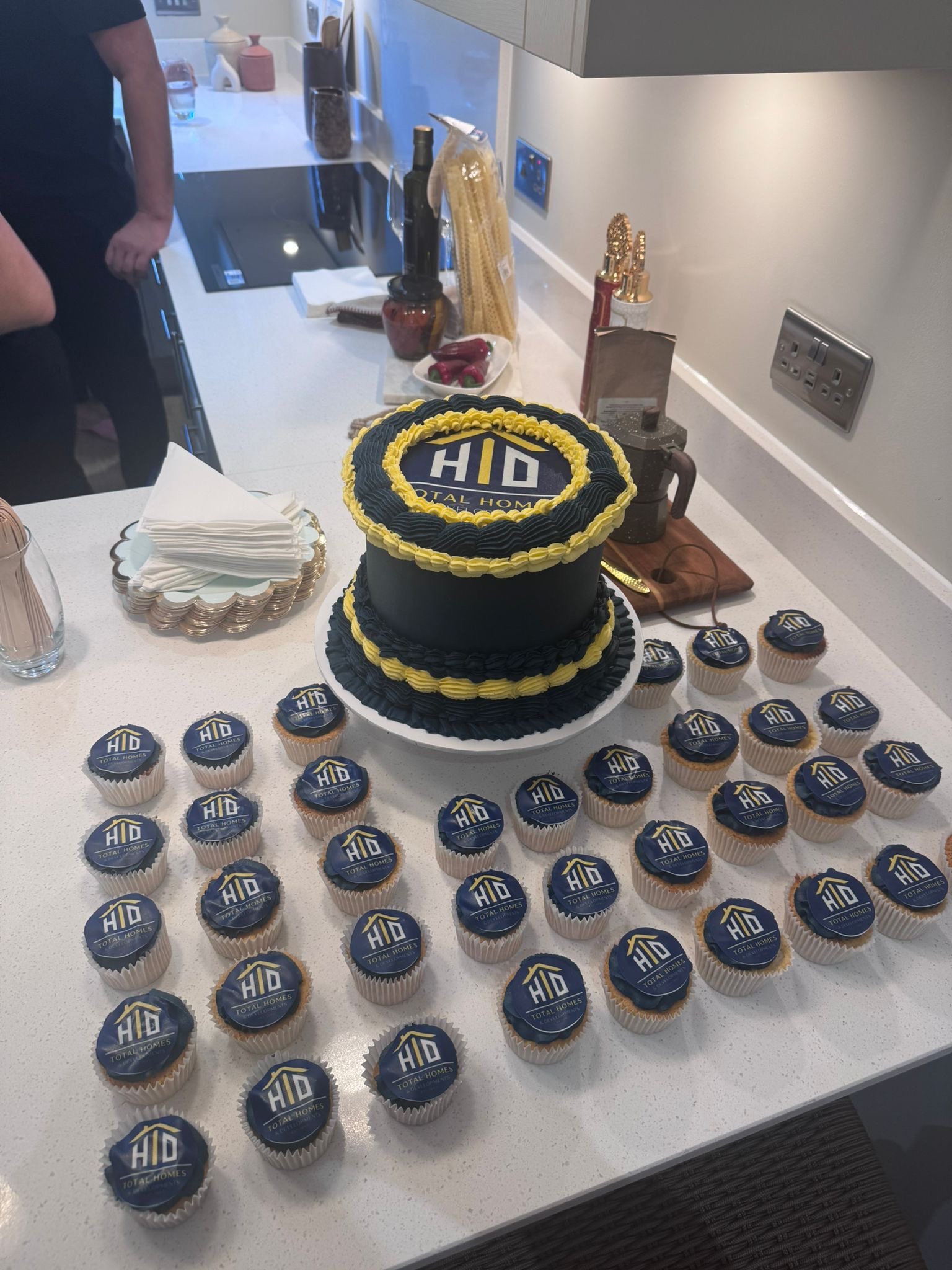 Celebration table with a cake and cupcakes featuring a logo for 'Total Homes', with a black and yellow color theme.