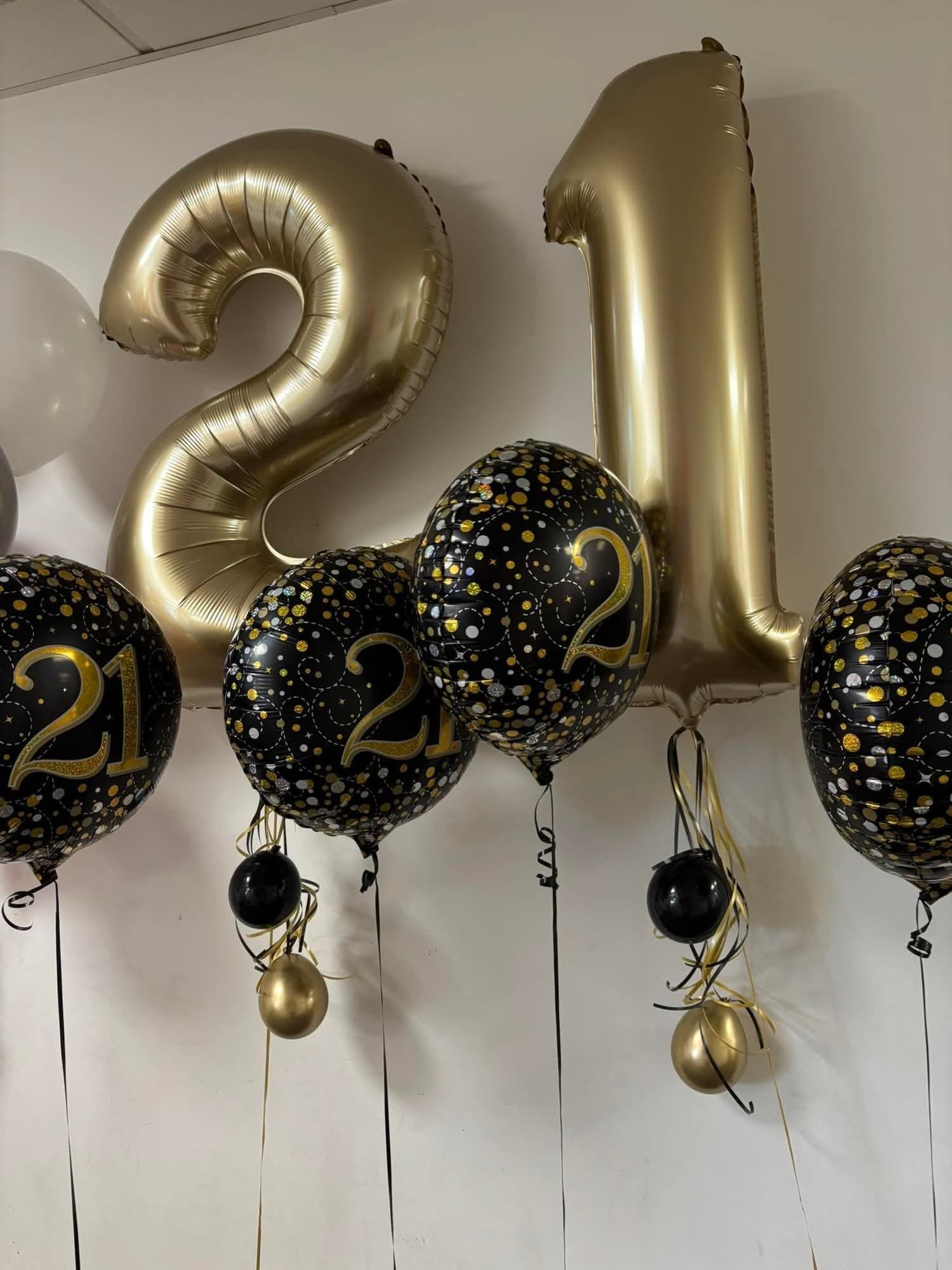 Gold number balloons forming '21' with black and gold themed balloons for a celebration.
