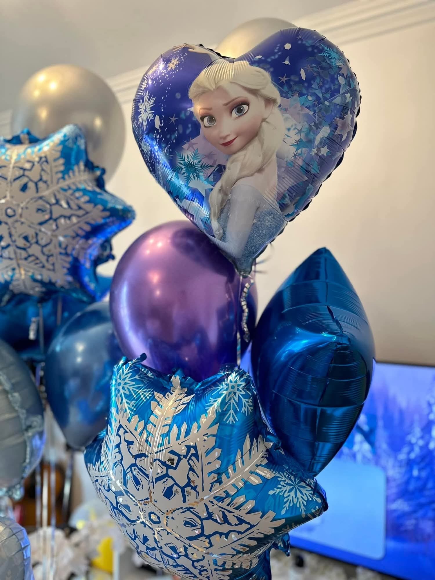 Balloon arrangement featuring a large heart-shaped balloon with Anna from Frozen, along with various star-shaped and round metallic balloons in blue, purple, and silver colors.