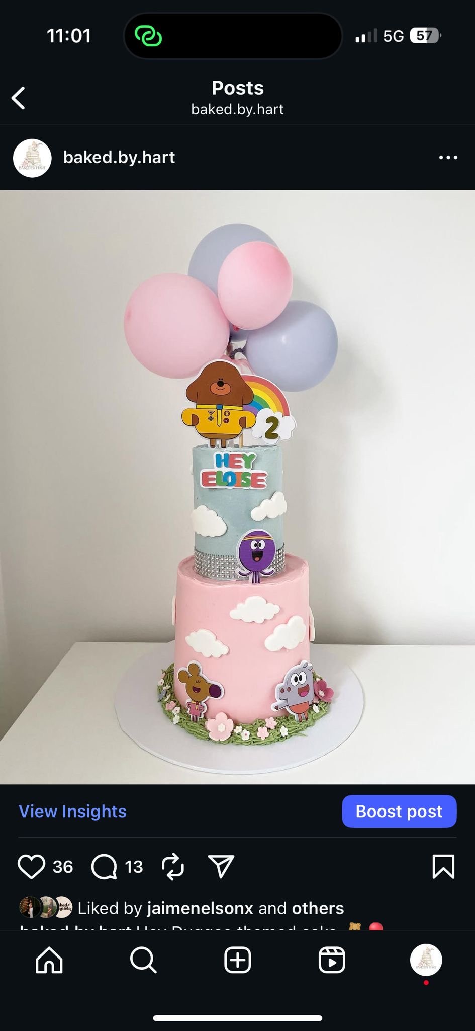 A two-tiered birthday cake with pastel pink and blue colors, decorated with clouds and cartoon character toppers, including a bear, a purple creature, and a gray mouse, with balloons on top.