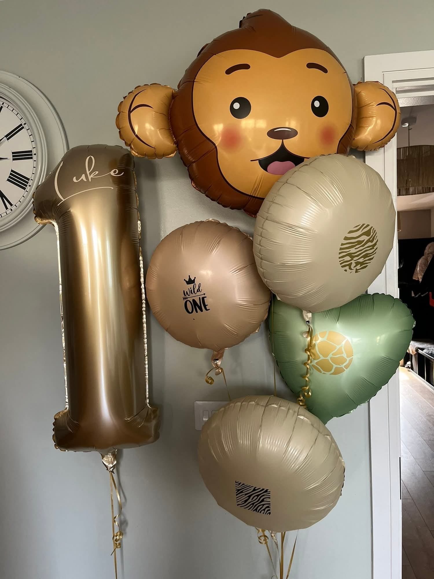 A collection of balloons for a first birthday celebration, including a large lion face balloon, a metallic number one balloon, and several round balloons with animal and celebration motifs.