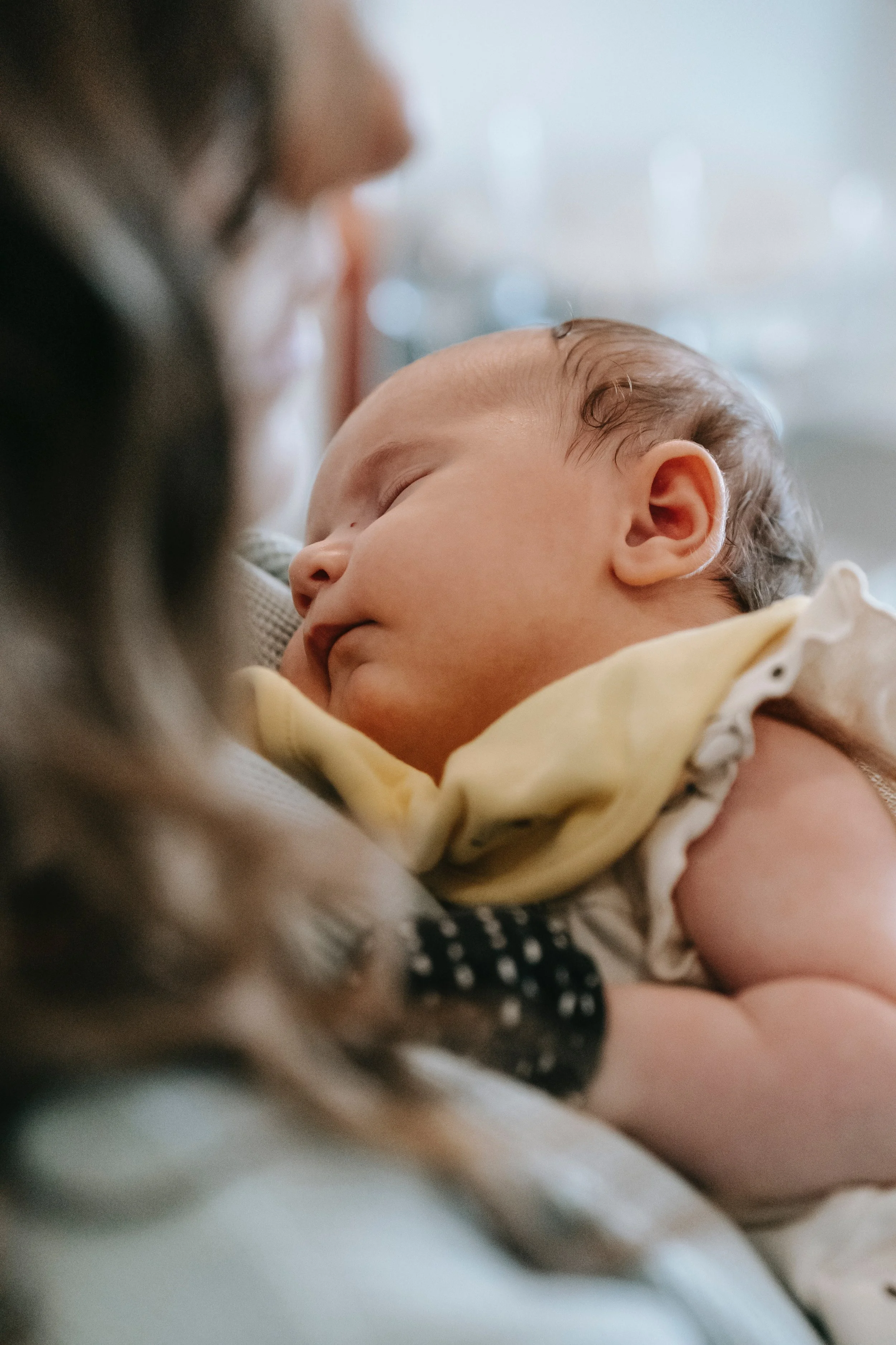 Close-up of a sleeping baby being held and cuddled by an adult, with the baby's face resting peacefully on the adult's chest.