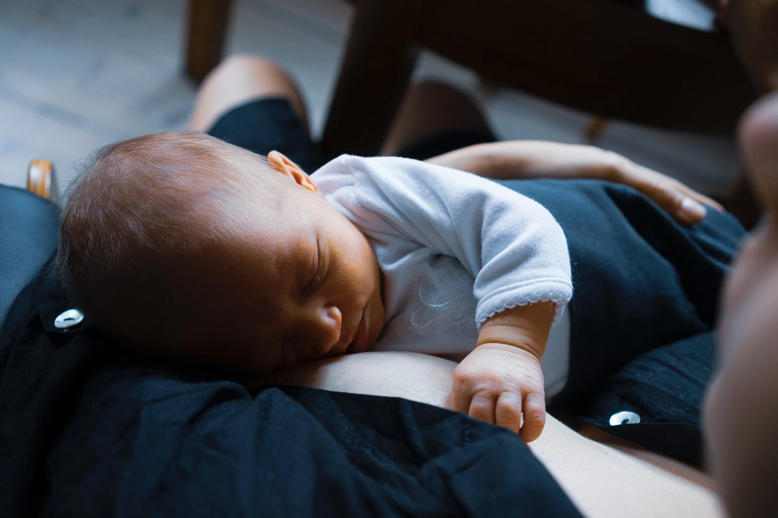 A newborn baby sleeping on a person's lap, with the person's legs visible and wearing dark shorts.