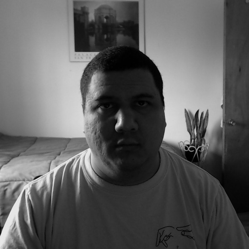 FLATTOP assis dans sa chambre, avec un lit et un tableau au mur, en noir et blanc.