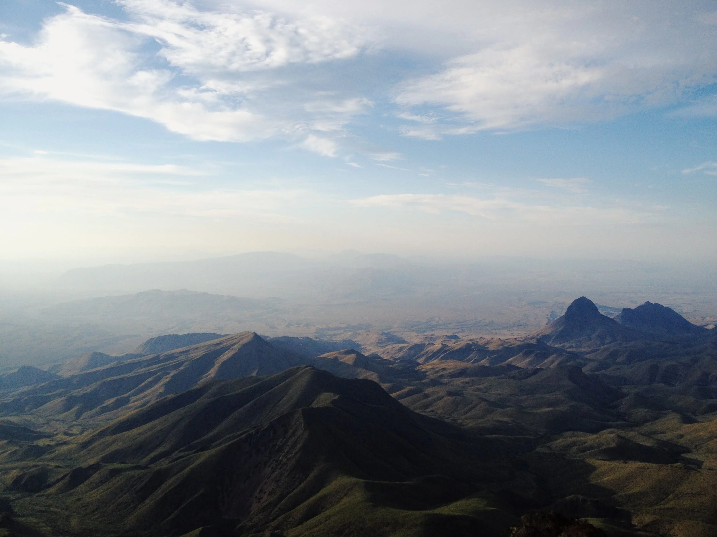 Mountain landscape with rolling green hills and rocky peaks under a daytime sky with some clouds.