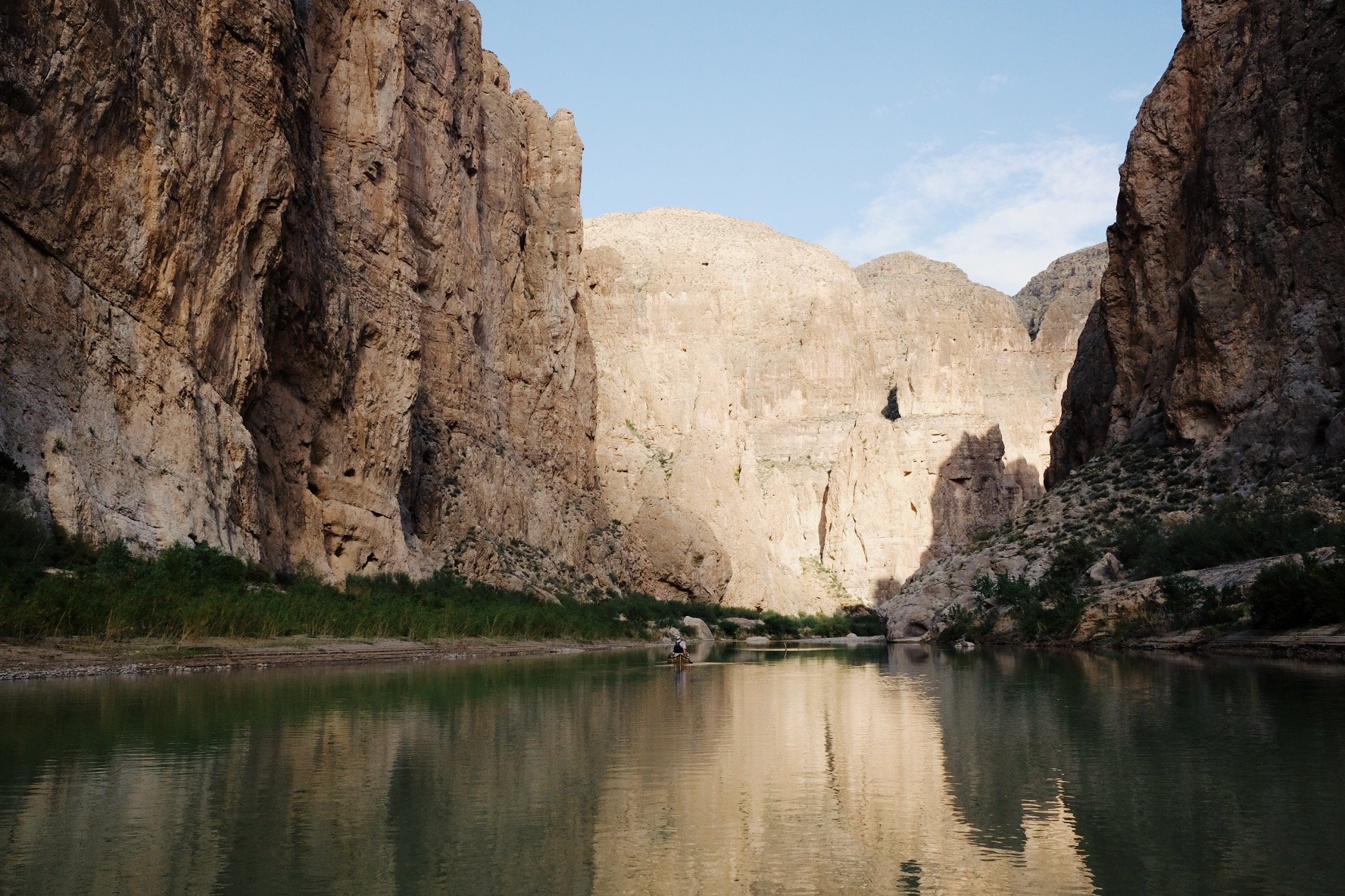 A narrow river flowing through a canyon with tall rocky cliffs on both sides and a person kayaking in the water.