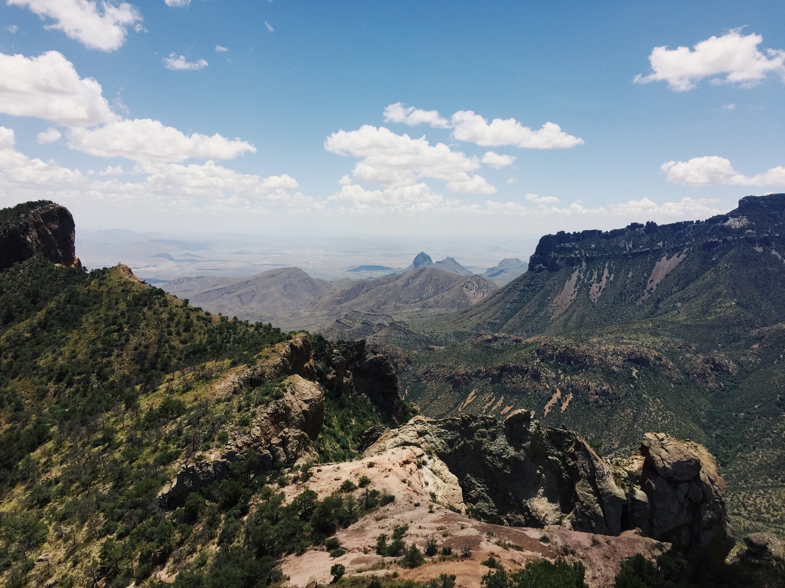 Mountain landscape with green vegetation, rocky cliffs, and a partly cloudy sky.
