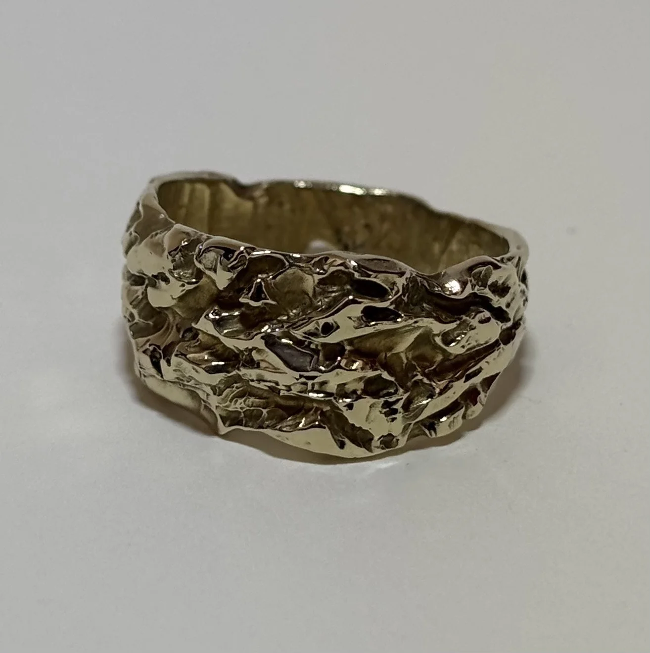 A gold ring with a textured, hammered design on a plain white background.