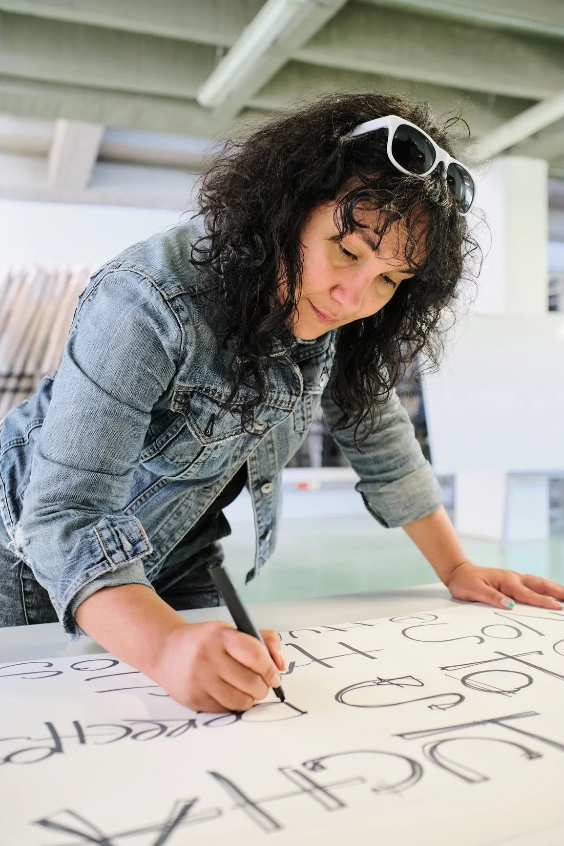 A light-skinned person with curly hair wearing a denim jacket, writing words on a protest sign.