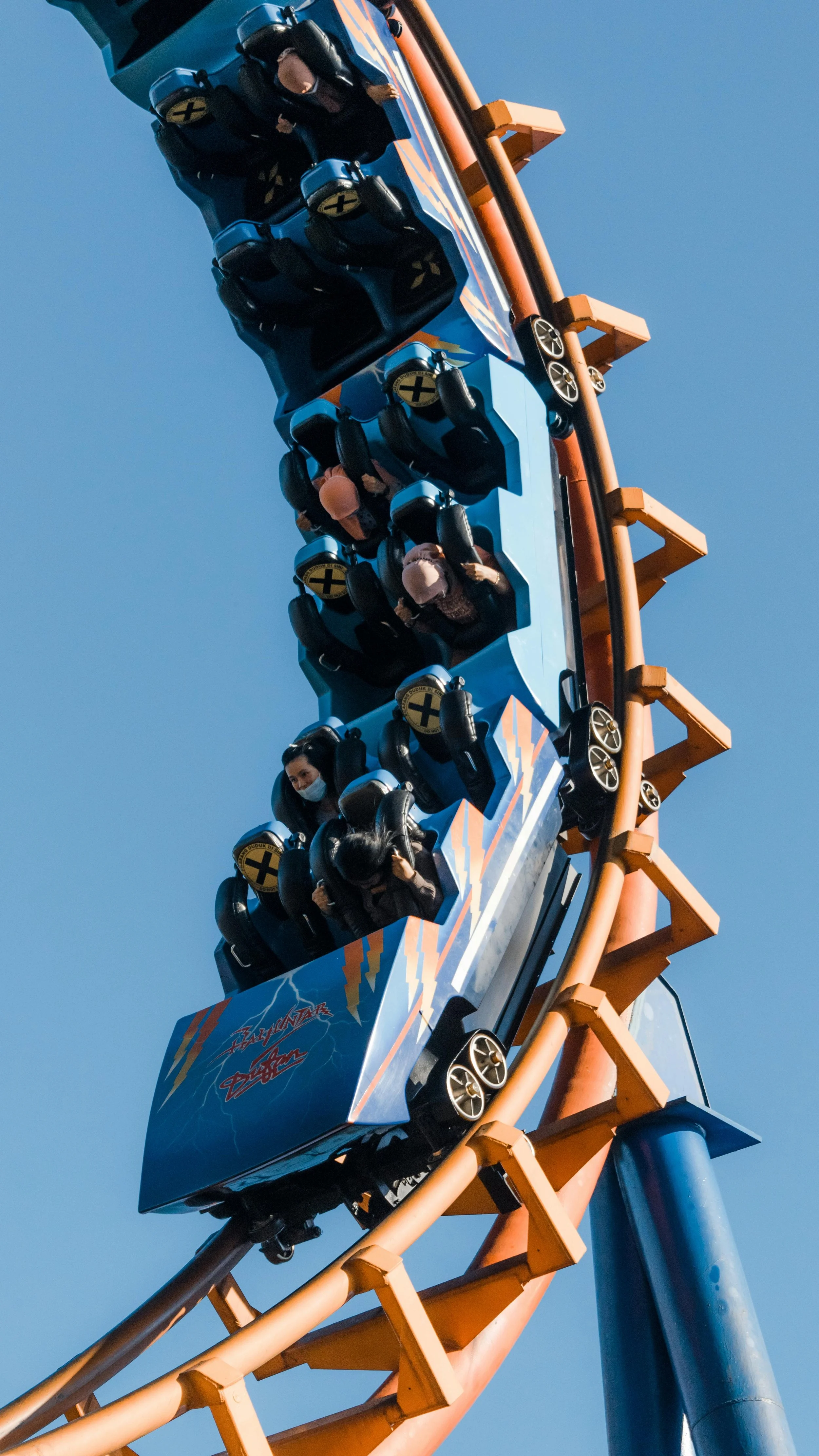 People riding a roller coaster ride in Legoland Billund, with some wearing face masks, on a bright sunny day.