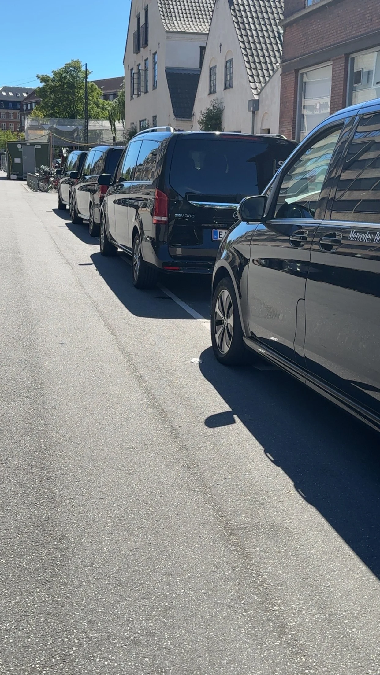 Line of parked Mercedes Vans on a Copenhagen street with buildings in the background under a clear blue sky ready for private transport to Billund Legoland.