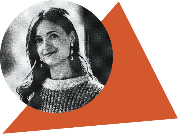 Black and white photo of a smiling woman with long hair, wearing a sweater and earrings, against a blurred background.