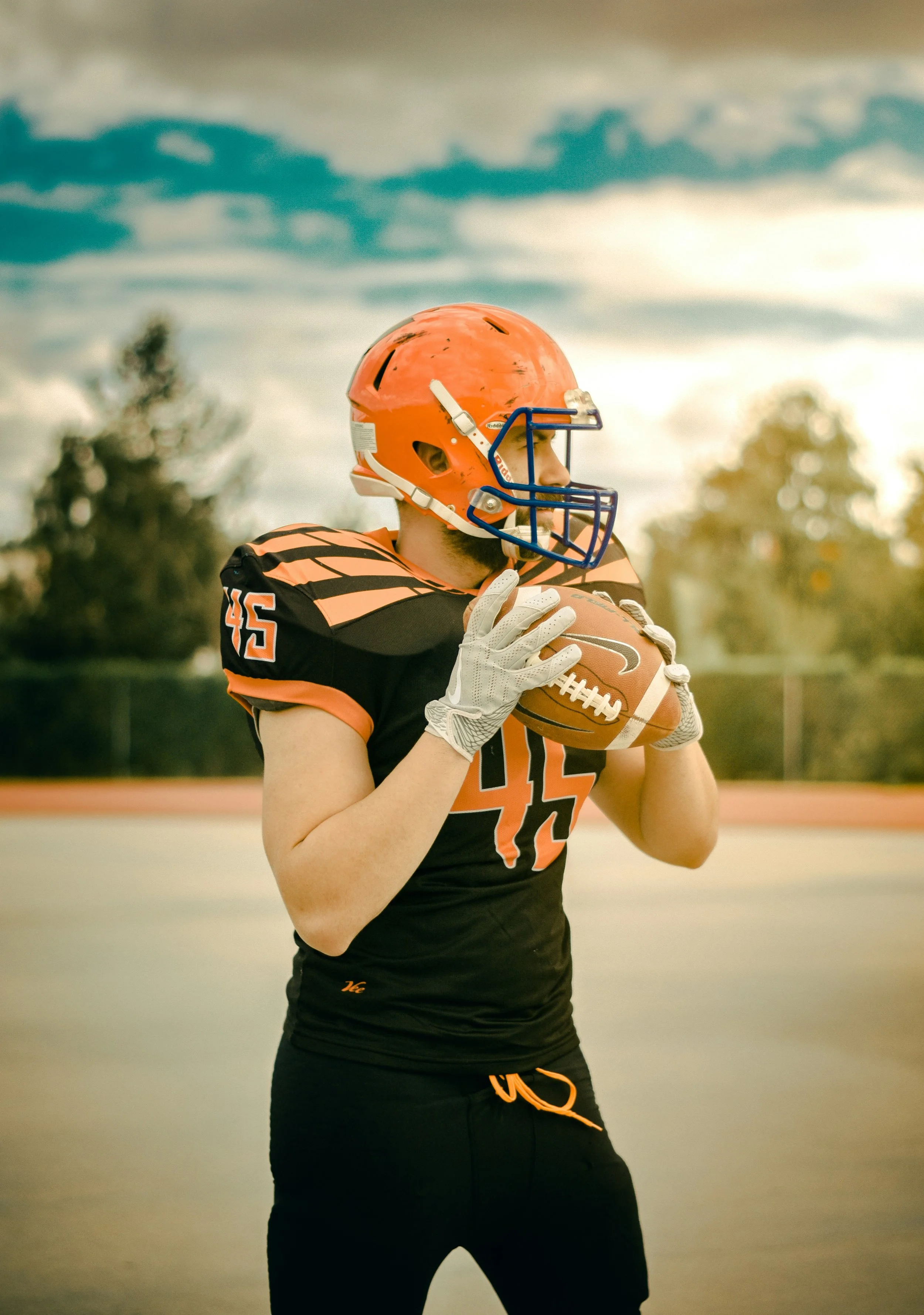 A football player in a black and orange uniform with a helmet and gloves, holding a football on an outdoor field.