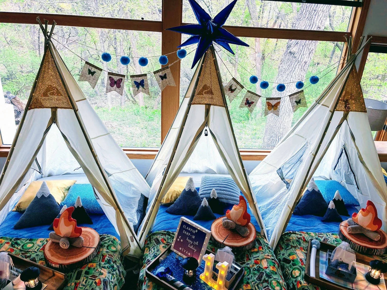 Kid size tent deocrated with campfire and mountain pillows, hiking gear and lantern with fuzzy blankets for birthday party sleepover glamping party