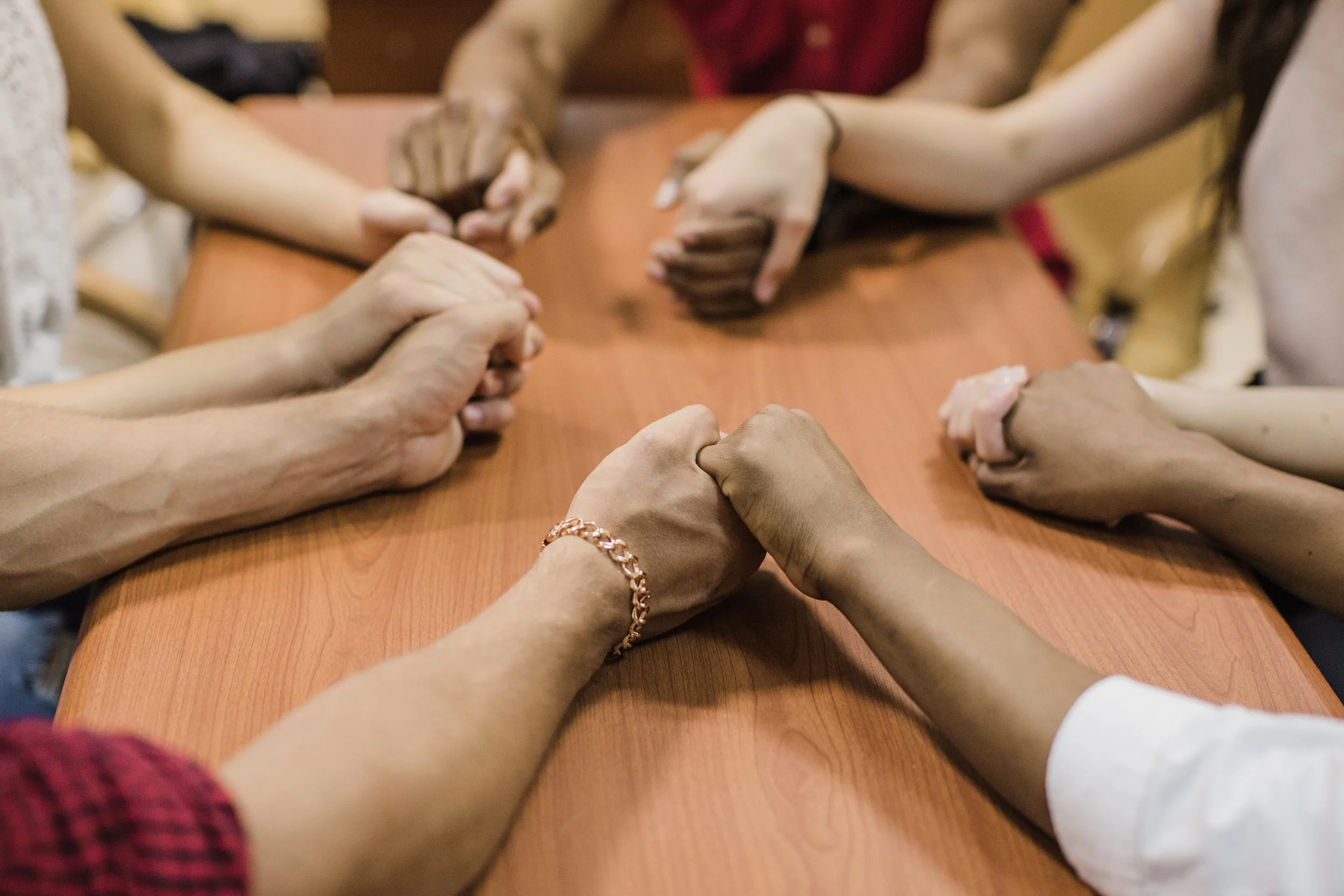 Multiple diverse hands clasped together in a show of unity over a wooden table.