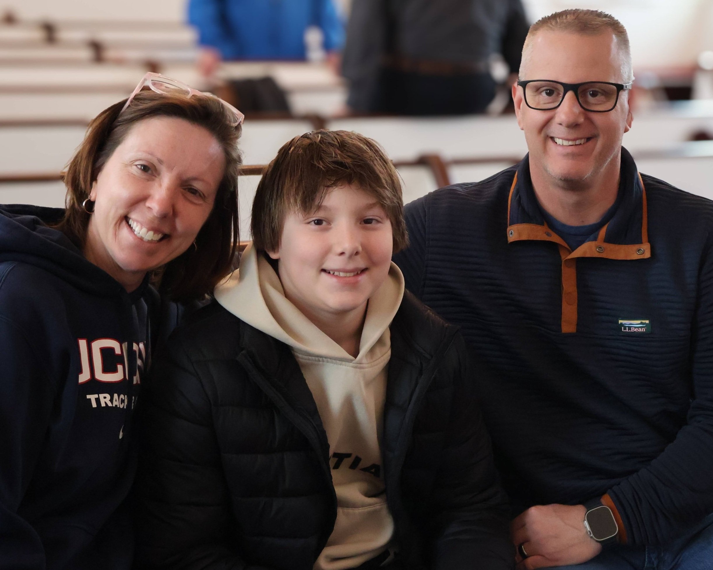 A smiling woman, boy, and man sitting close together in a stadium or auditorium, posing for a photo.
