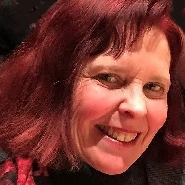Close-up of a woman with shoulder-length red hair smiling and looking at the camera.