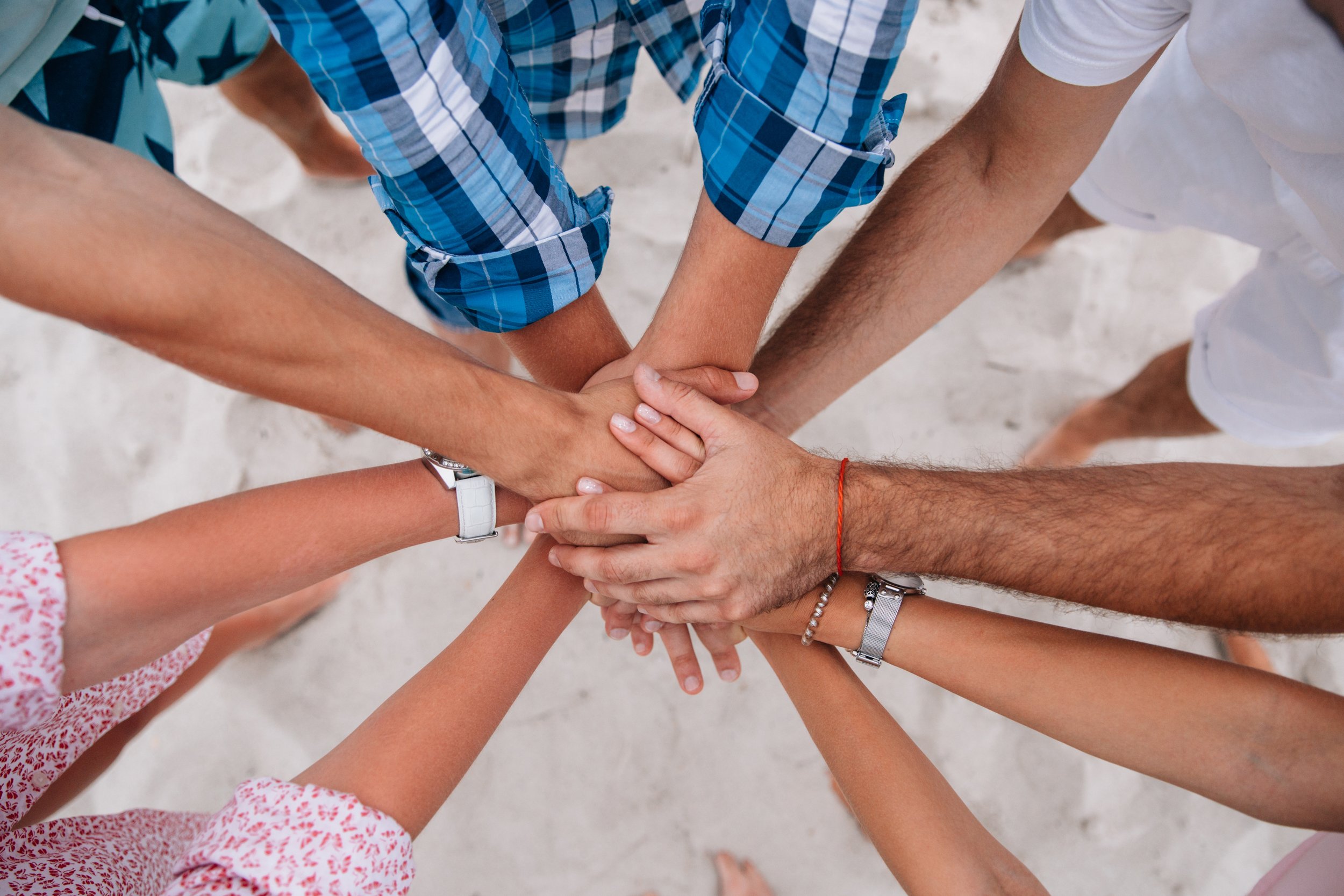 Group of people on a beach putting their hands together in a unity gesture.