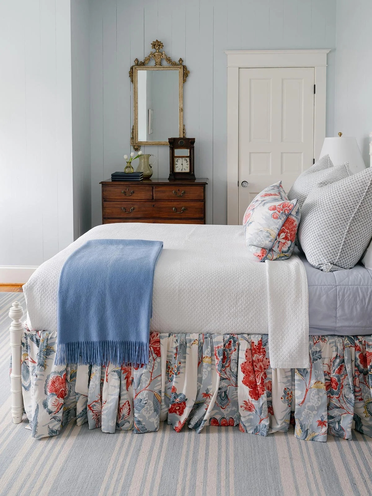 Guest bedroom designed by Elizabeth Hartz Interior Design at The River home in Kilmarnock, Virginia. Features a four-poster bed with floral textiles, soft blue walls, antique dresser, and gold mirror, combining coastal charm with classic Southern ele