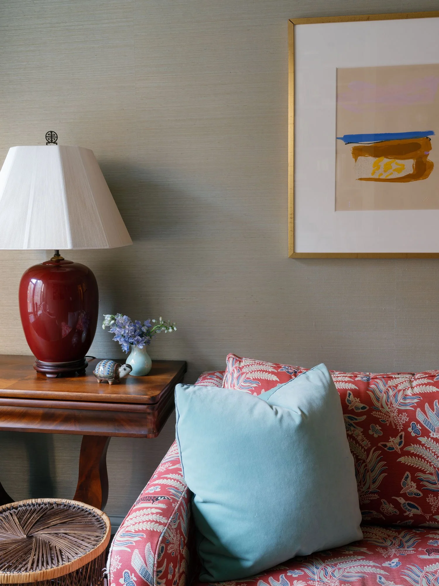 New York City apartment sitting area by Elizabeth Hartz Interior Design featuring patterned sofa, blue accent pillow, vintage wood side table, sculptural table lamp, and framed abstract artwork.