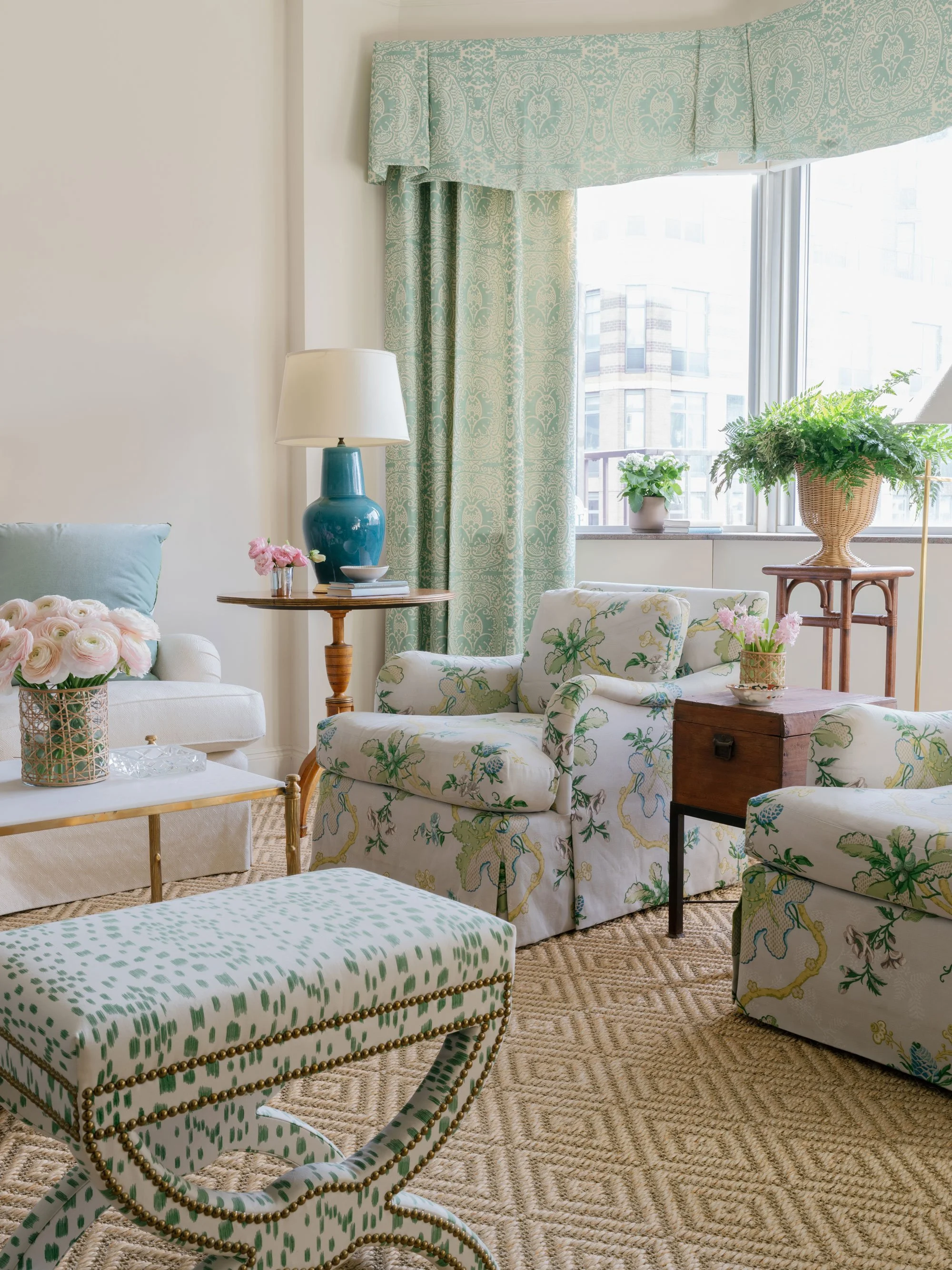 Bright New York City living room with cream sofa, patterned green drapery, floral armchair, marble coffee table, and layered pastel accents styled in a classic, timeless aesthetic.
