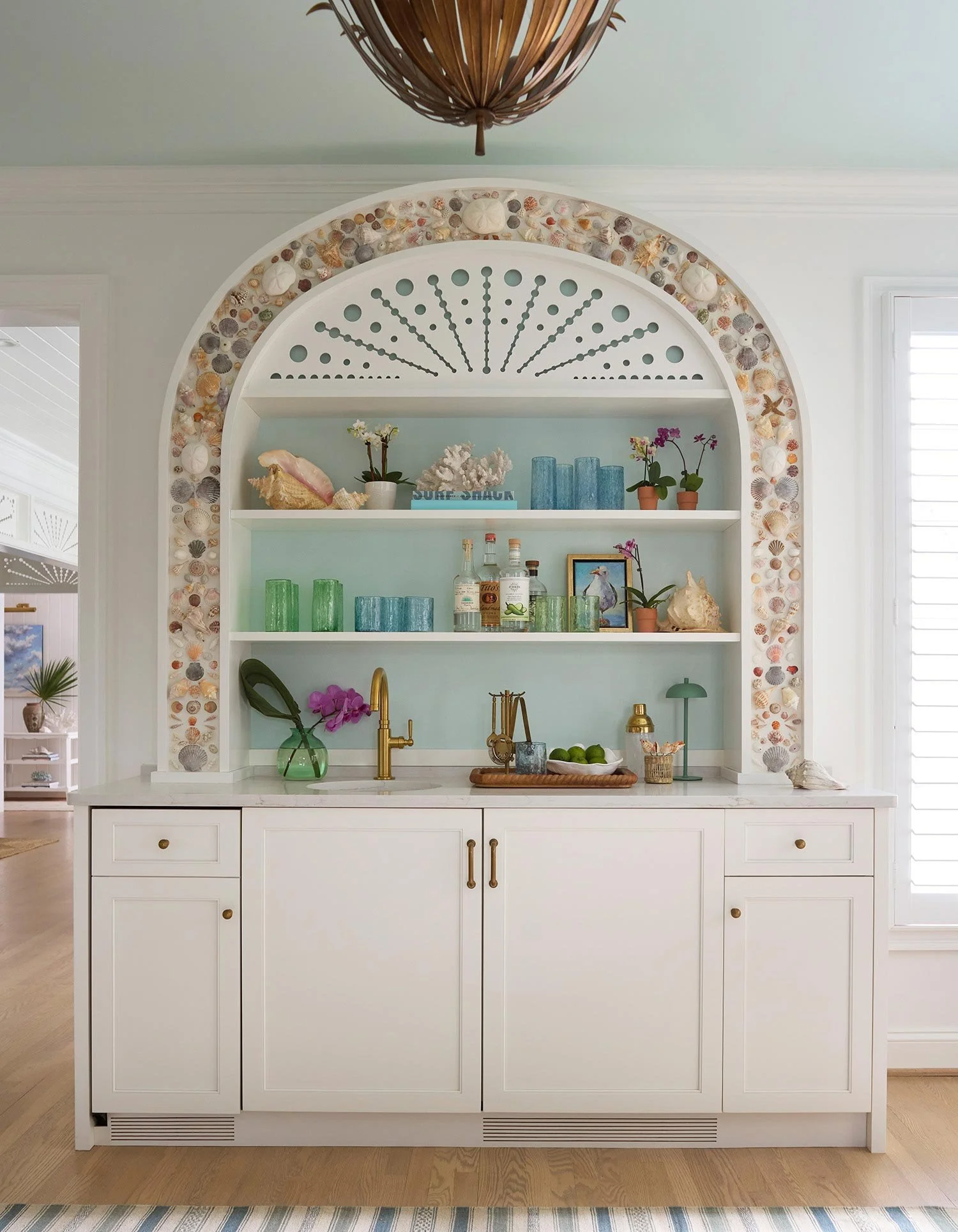 Elizabeth Hartz interior designer Virginia Beach custom shell bar with built-in cabinetry, arched niche detailed in seashells, soft coastal blue backdrop, and refined oceanfront styling