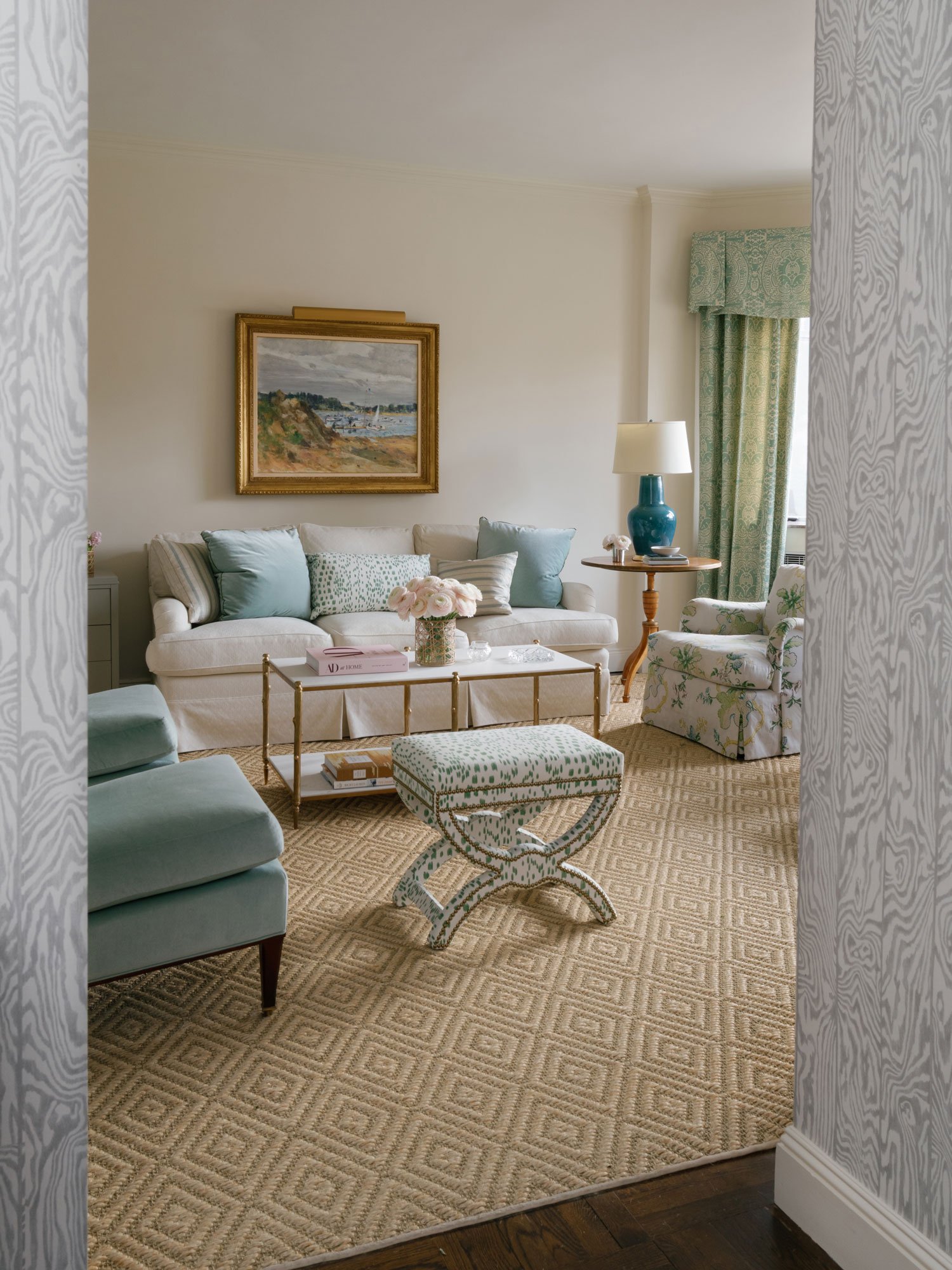 Wide view of living room in New York City apartment by Elizabeth Hartz Interior Design featuring tailored sofa, patterned accent chairs, soft blue and green textiles, brass coffee table, woven area rug, and layered southern-inspired styling with clas