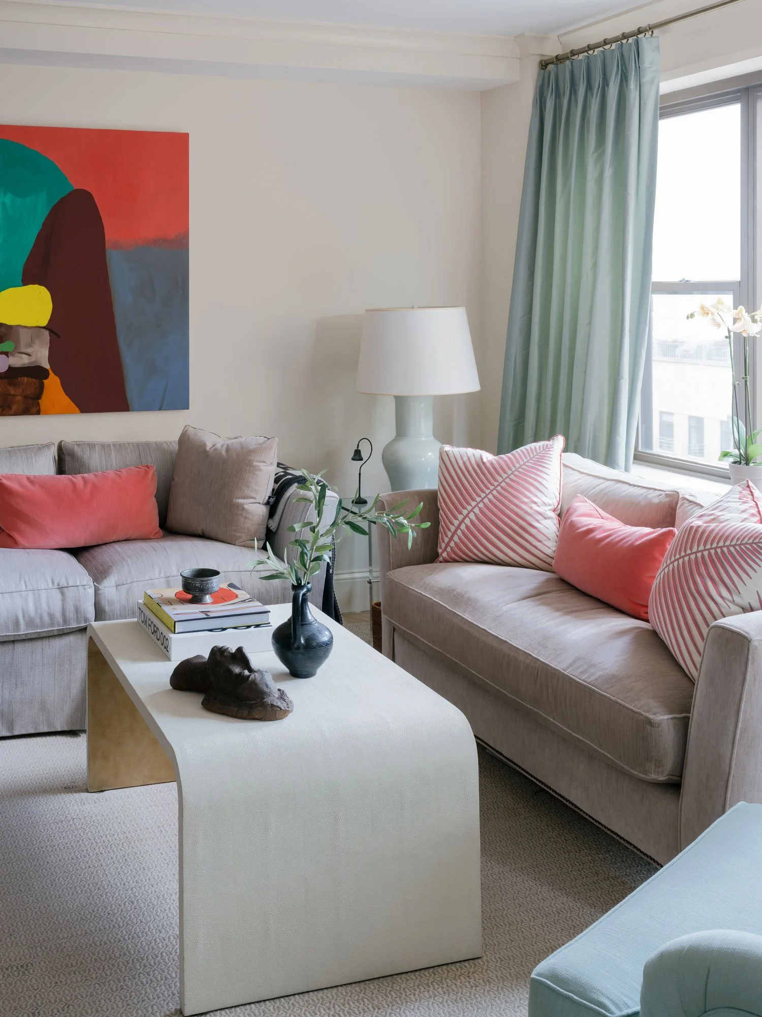 New York City living room interior design by Elizabeth Hartz Interior Design featuring layered neutral sofas, coral accent pillows, sculptural coffee table, abstract artwork, and soft green drapery.