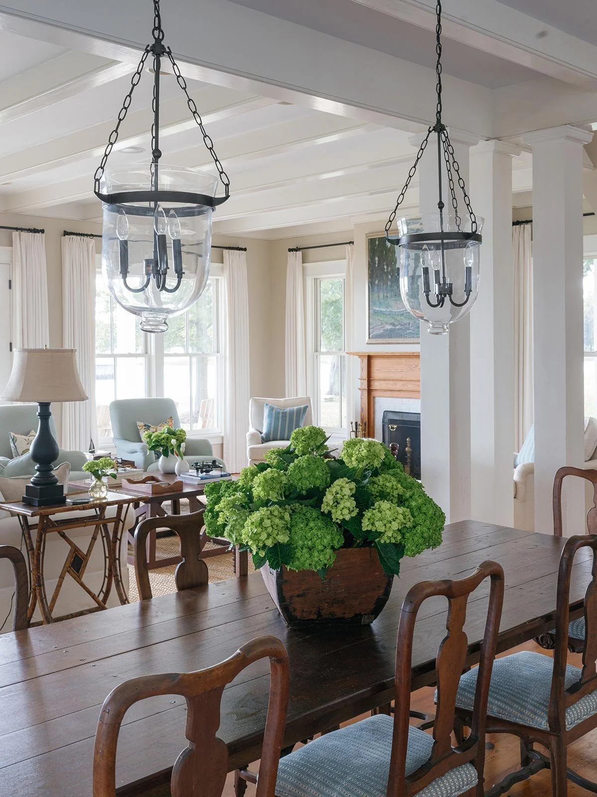Open-concept dining and living area designed by Elizabeth Hartz Interior Design at The River home in Kilmarnock, Virginia. A dark wood dining table with green hydrangeas overlooks a bright sitting room with coastal tones, natural textures, and elegan