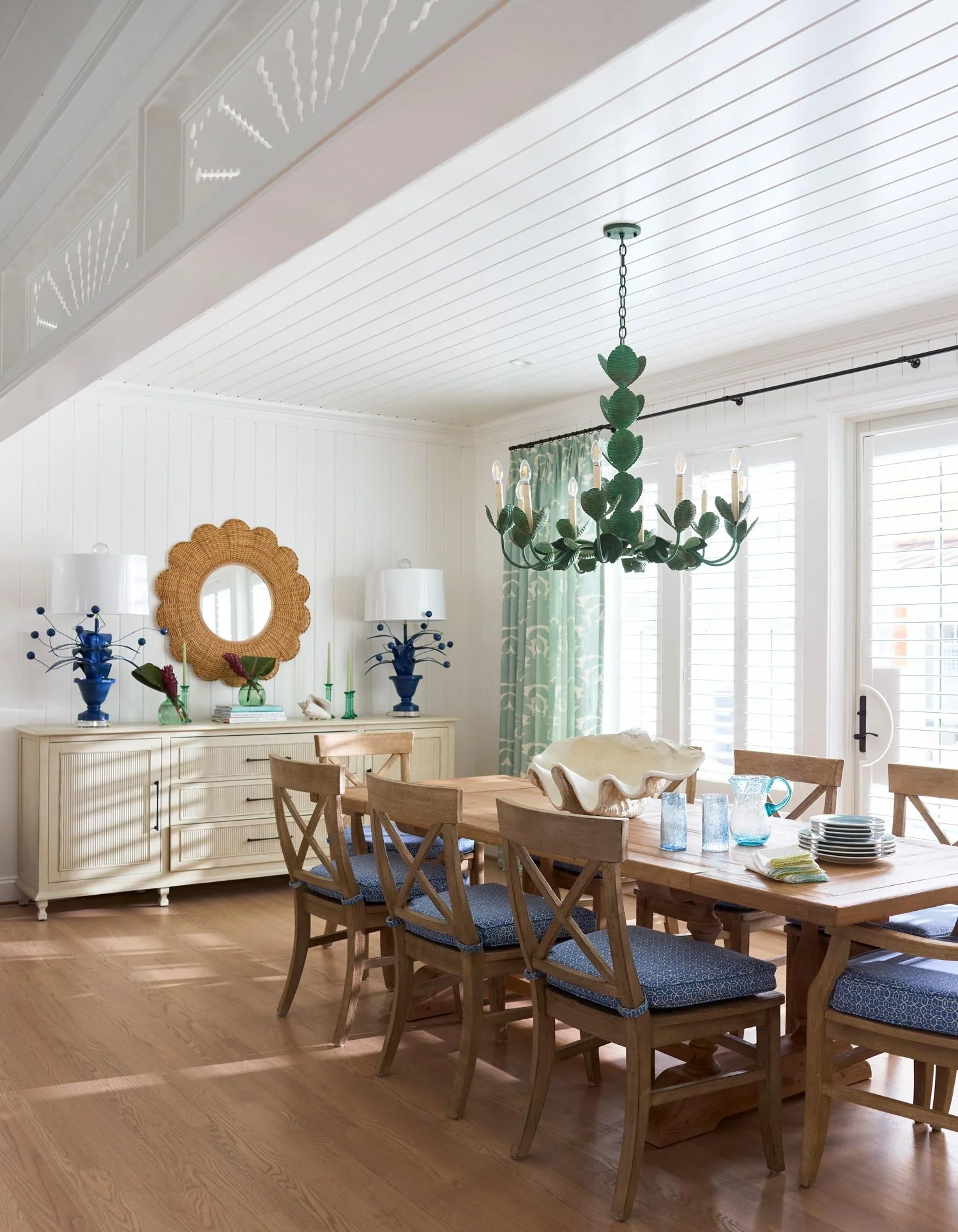 Elizabeth Hartz interior designer Virginia Beach dining room with coastal wood table, woven chairs, shell centerpiece, green statement chandelier, and soft blue accents in a Palm Beach–inspired oceanfront home