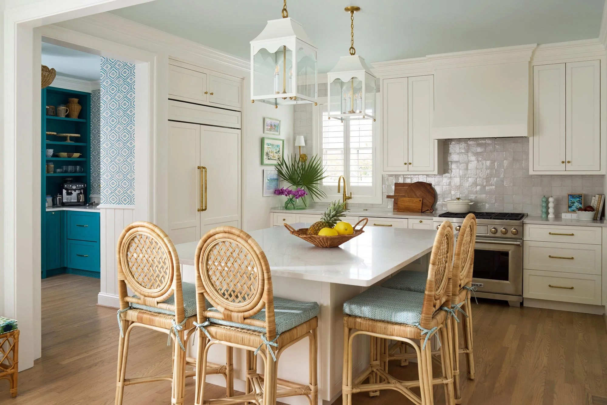 Elizabeth Hartz interior designer Virginia Beach oceanfront kitchen with white cabinetry, marble island, woven rattan bar stools, brass accents, and a connected blue coffee bar in a refined coastal style
