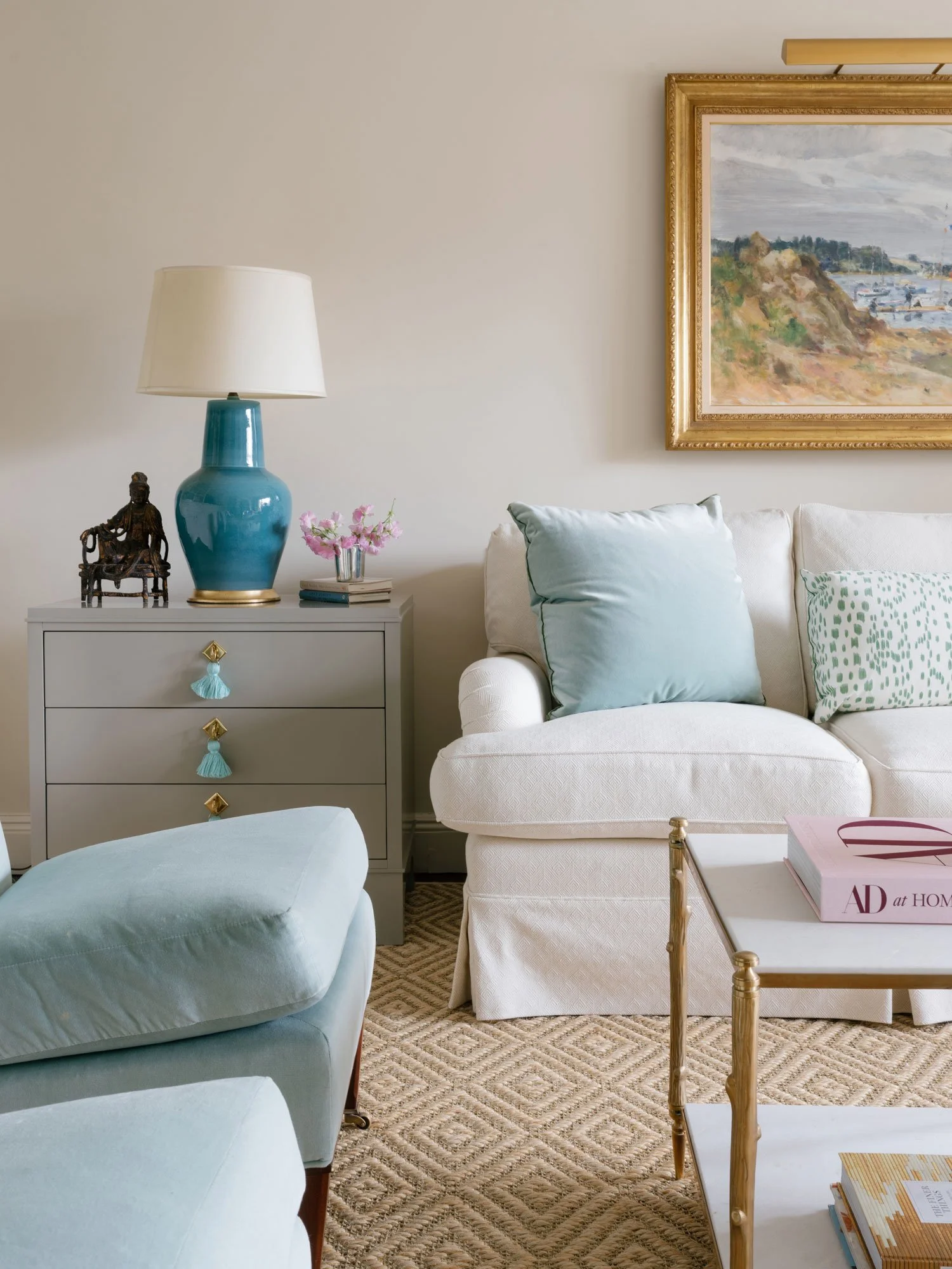 New York City apartment living room seating vignette by Elizabeth Hartz Interior Design showcasing a soft neutral sofa, pale blue accent chair, ceramic table lamp, tailored pillows, and classic artwork in a layered, southern-influenced interior.