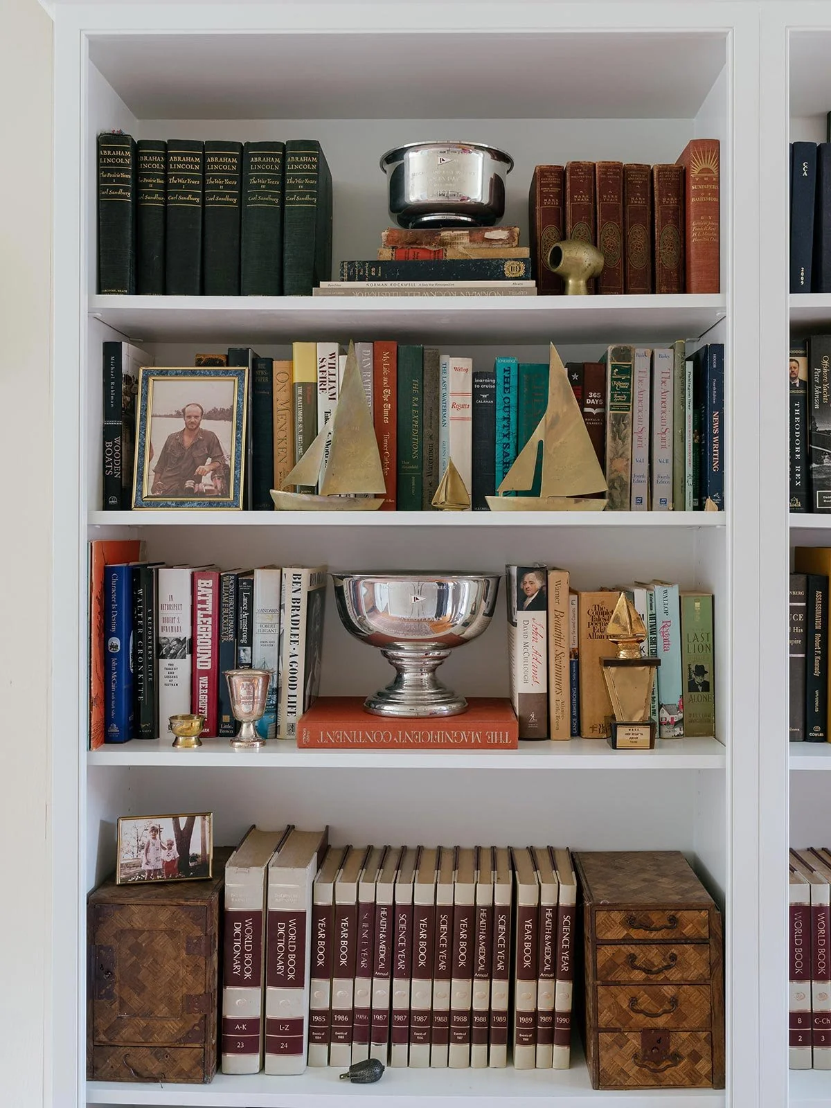 Curated bookshelf styled by Elizabeth Hartz Interior Design at The River home in Kilmarnock, Virginia. Features vintage books, brass sailboat sculptures, silver trophies, and personal family photos, reflecting a collected, coastal-inspired interior w