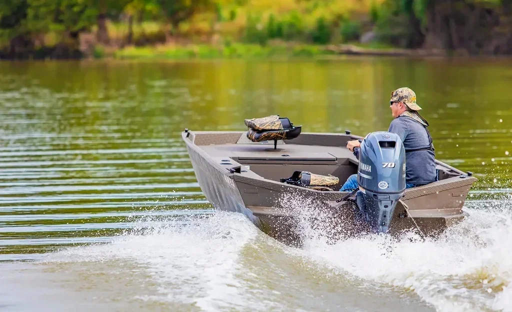 Rear view of a small aluminum alweld fishing boat with a Yamaha outboard motor speeding across a green lake.