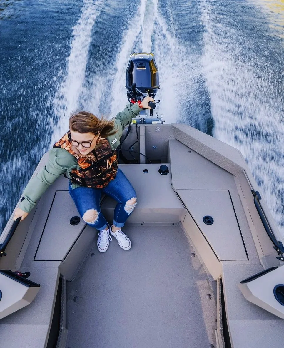 Person seated inside a small aluminum alweld boat holding onto the side as the Yamaha outboard motor powers through the water, leaving a wake behind.