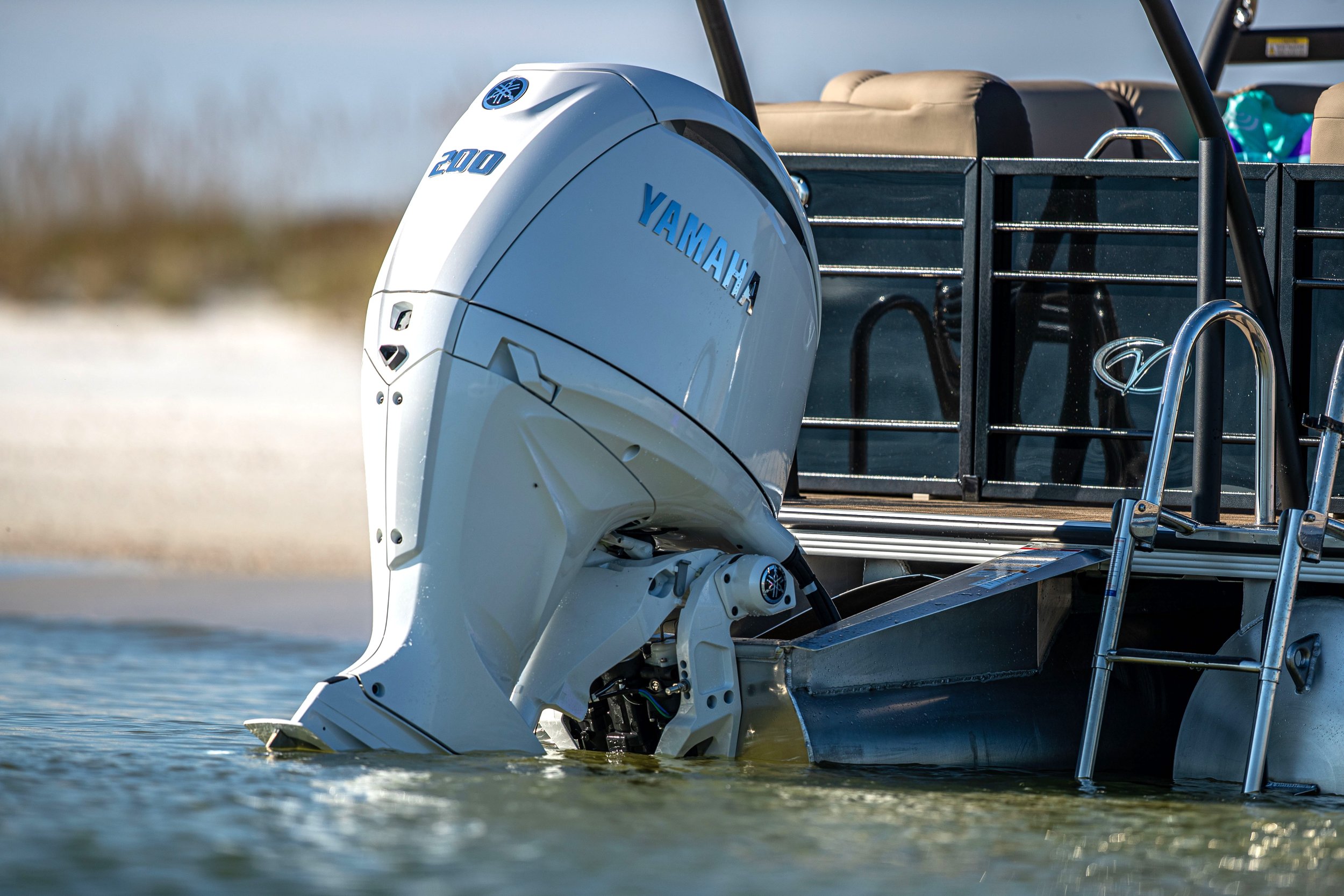 Close-up of a Yamaha outboard motor attached to a boat, partially immersed in water, with beige seats and a metal ladder visible on the boat.