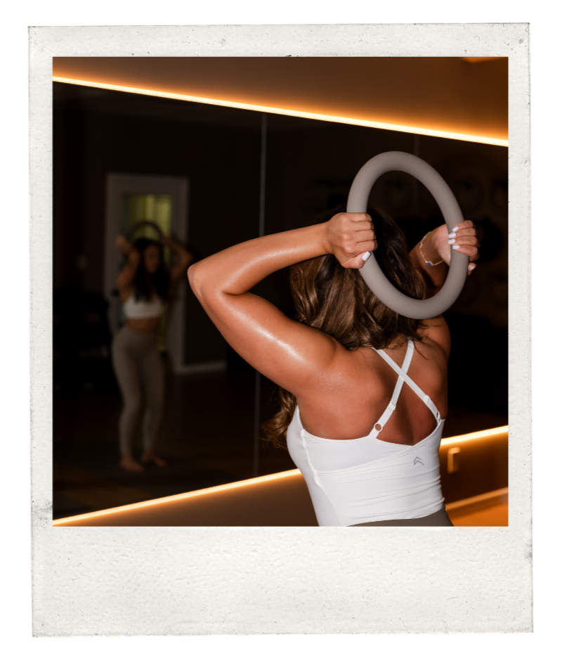 Woman exercising with a fitness ring in front of a mirror in a gym.