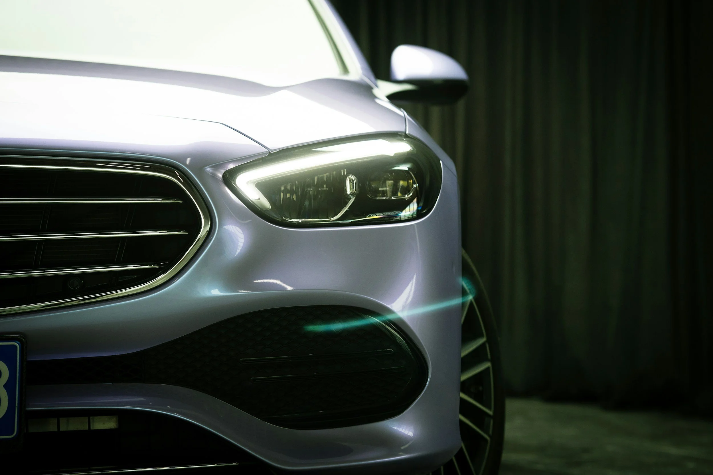 Close-up of the front of a silver luxury car with its headlight turned on.