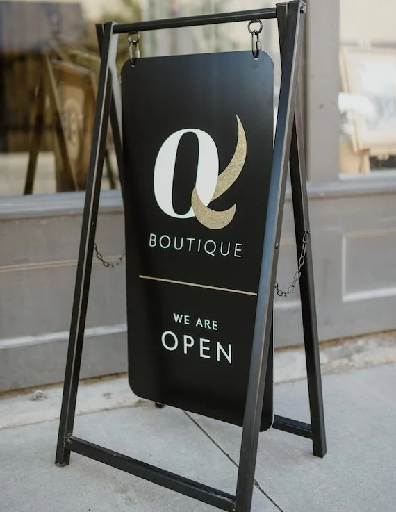 A black A-frame with hung composite panel open sign.