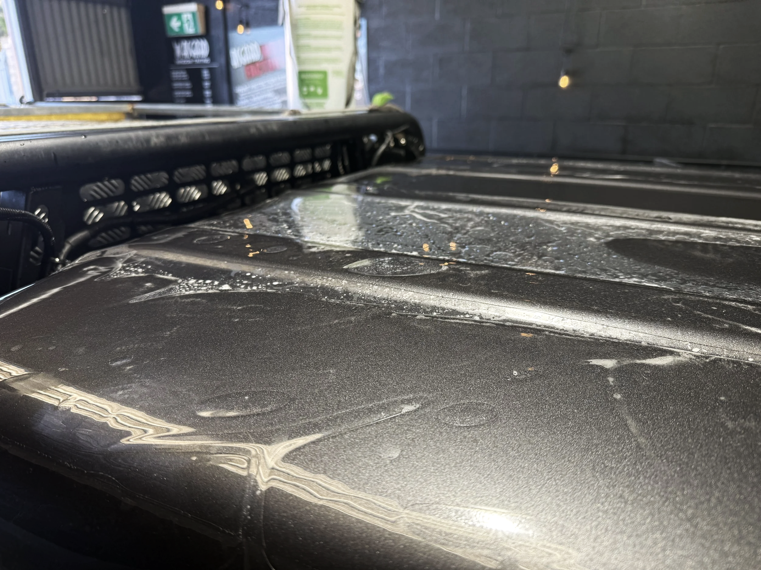 Close-up of a dusty, dirty black surface, possibly a vehicle hood, with specks of dust and smudges visible.