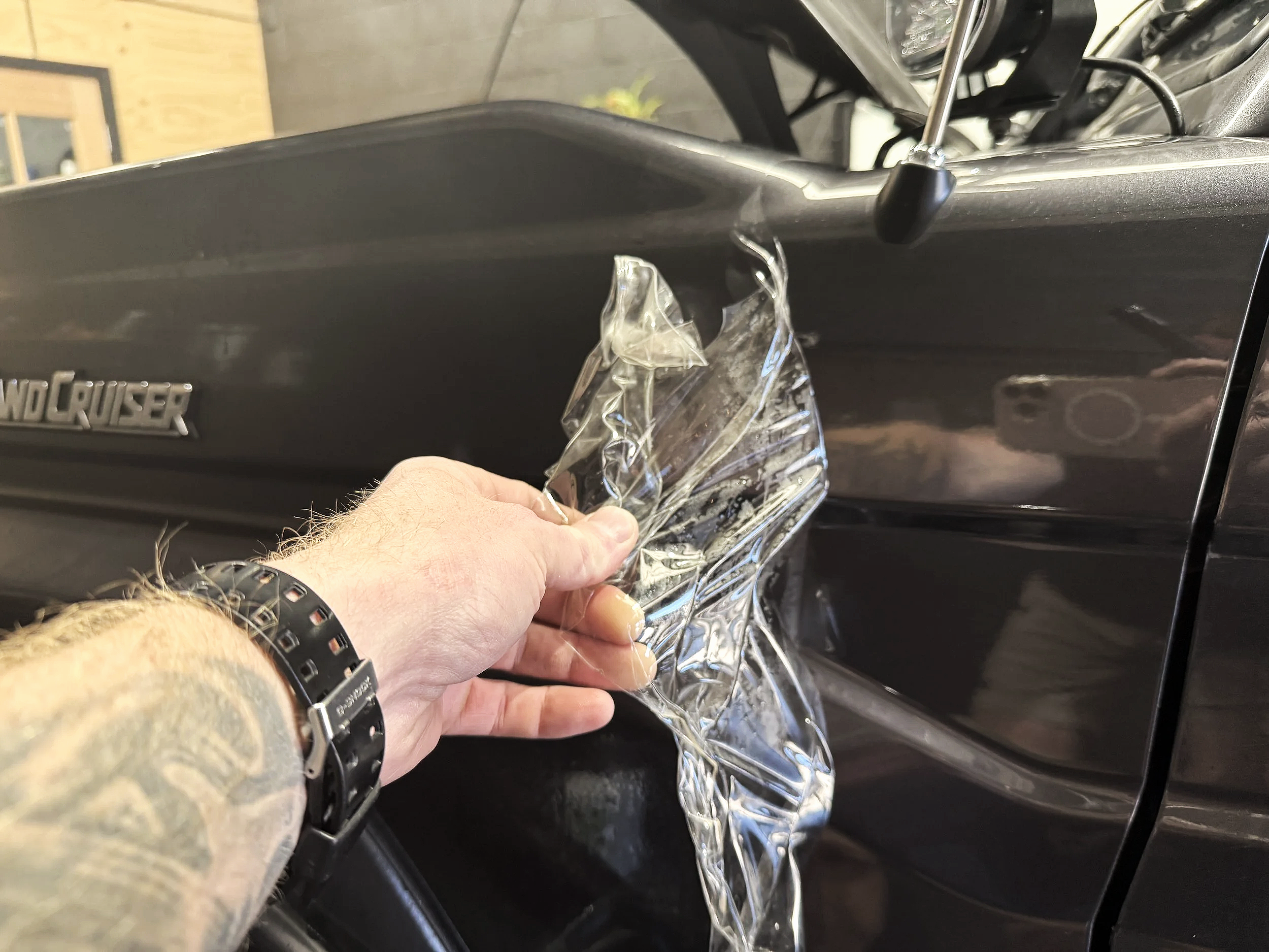 A person peeling off a protective plastic film from the side of a black Toyota Land Cruiser.