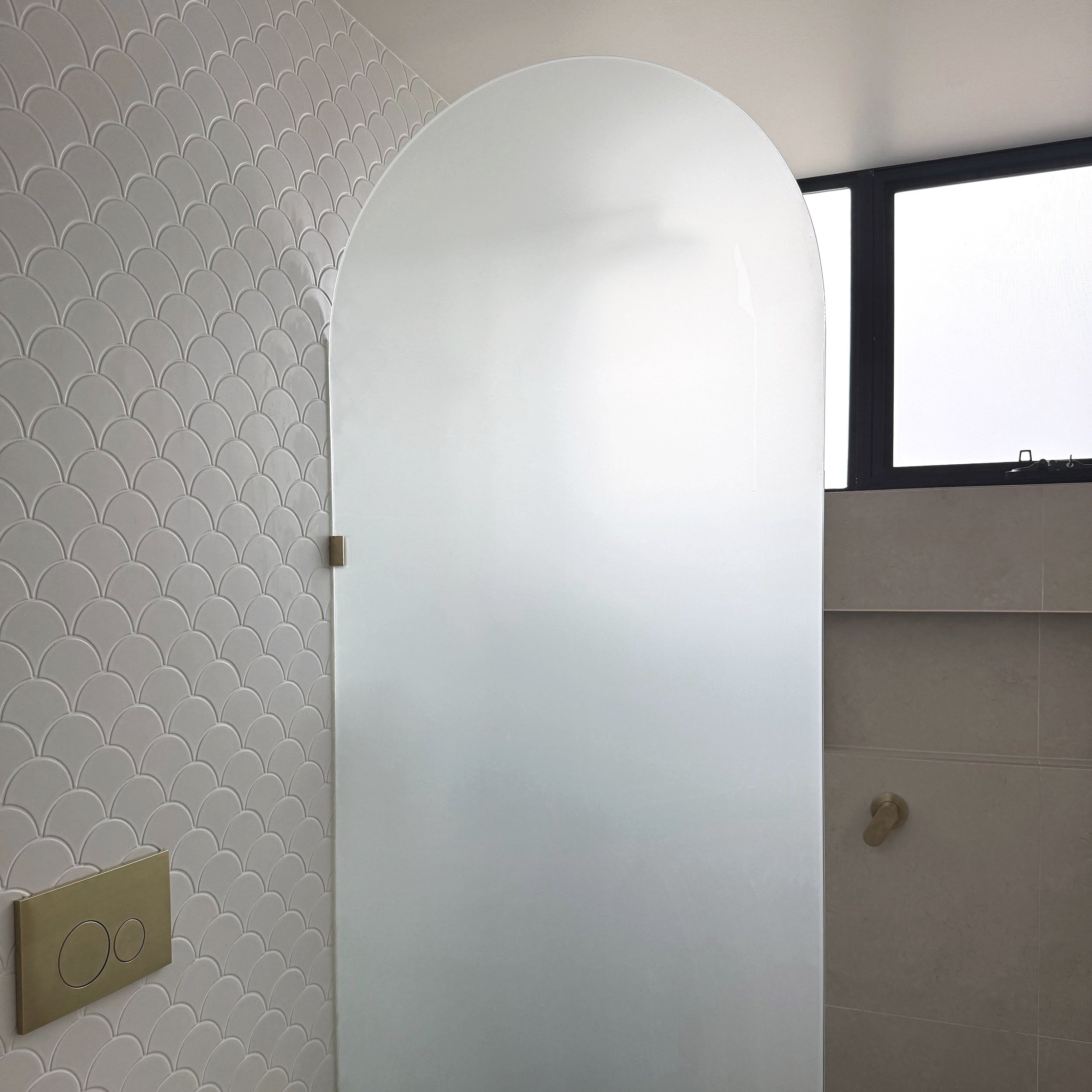 A modern bathroom with a frosted glass arch shower screen.