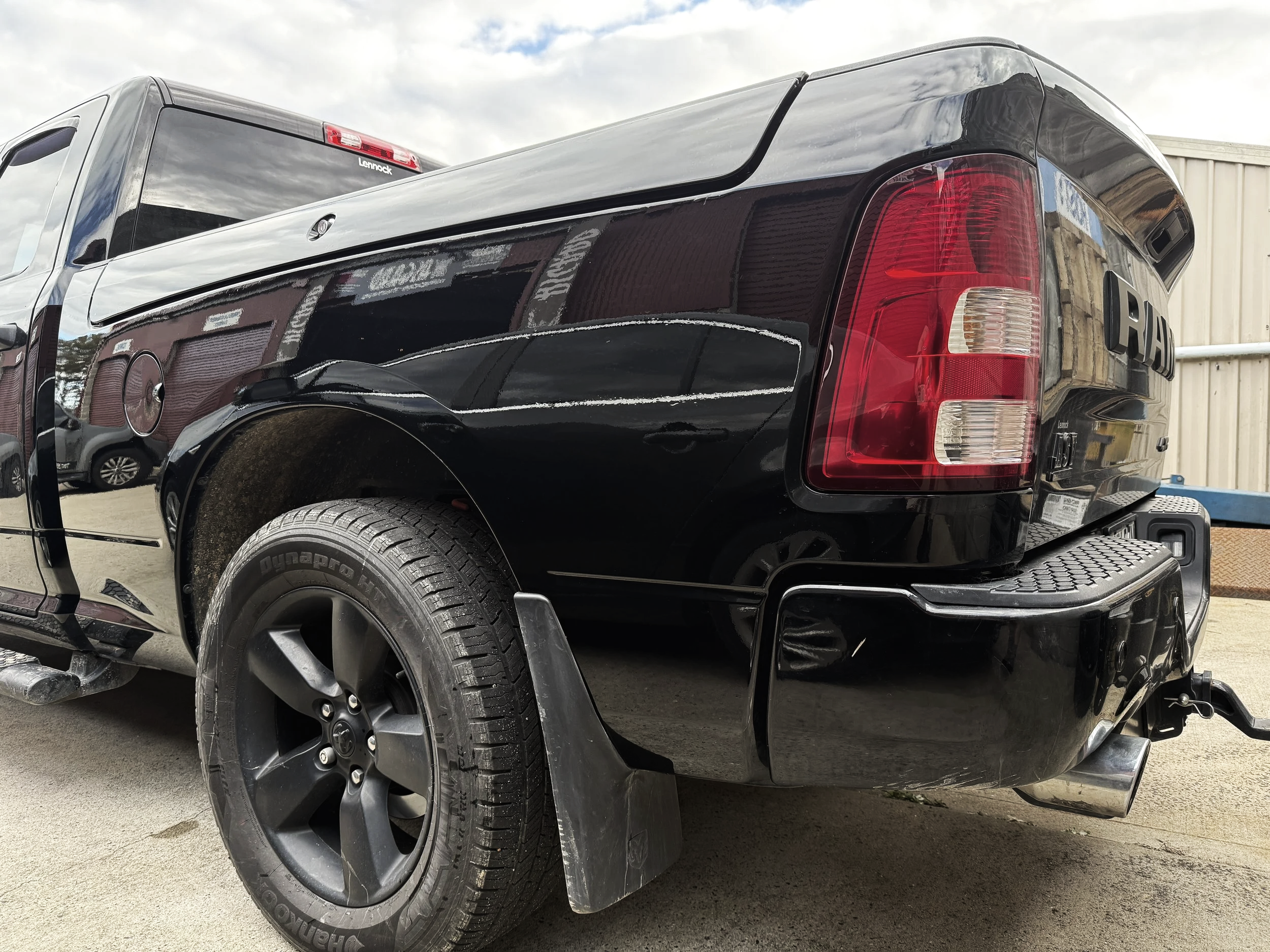 Rear view of a black pickup truck with visible tools in the truck bed and a trailer hitch, parked outdoors near an industrial building.