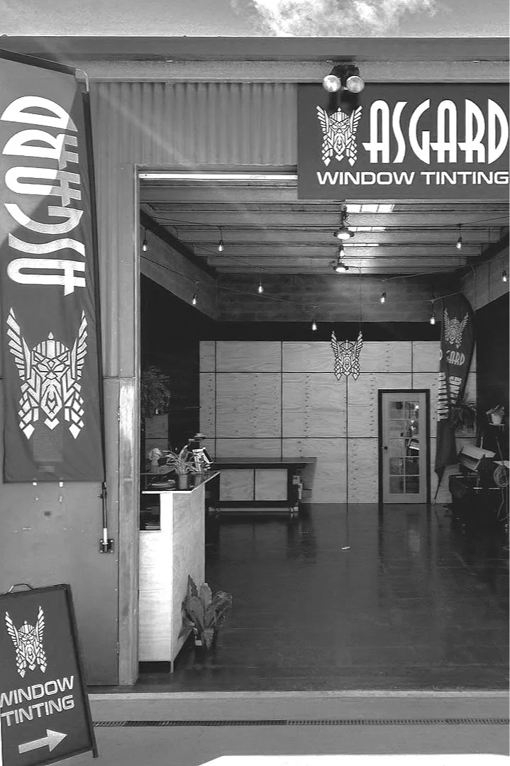 Interior of a window tinting shop called Asgard with banners and signage, featuring a reception area, a door, and decorative lighting.