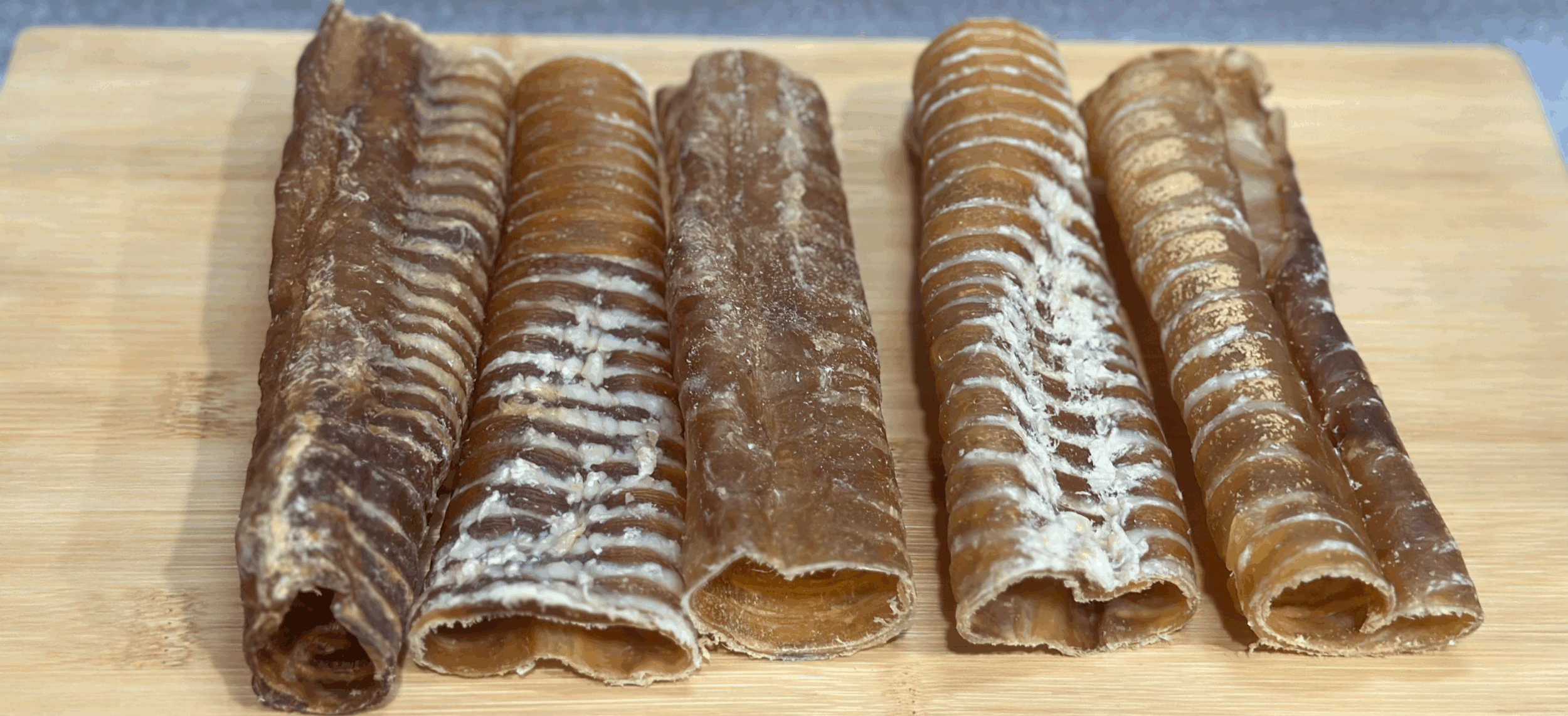 Six dehydrated beef tracheas on a wooden cutting board.