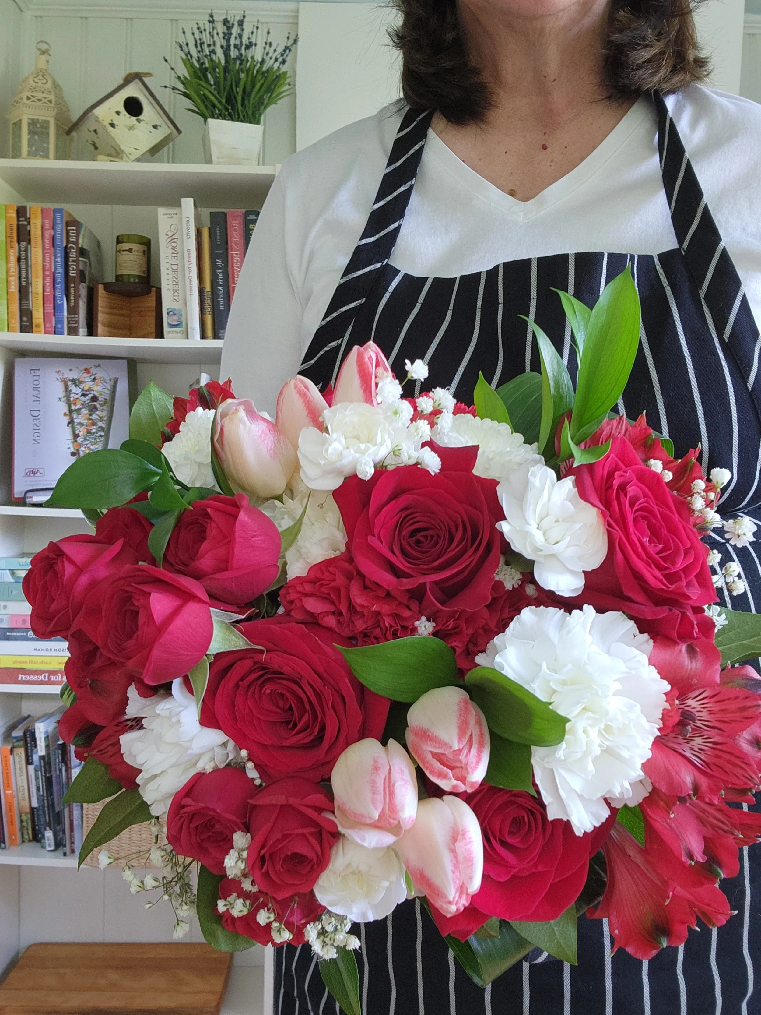Carrie, the owner of Bloom Wildly, holding a vibrant red and white floral bouquet in her studio.