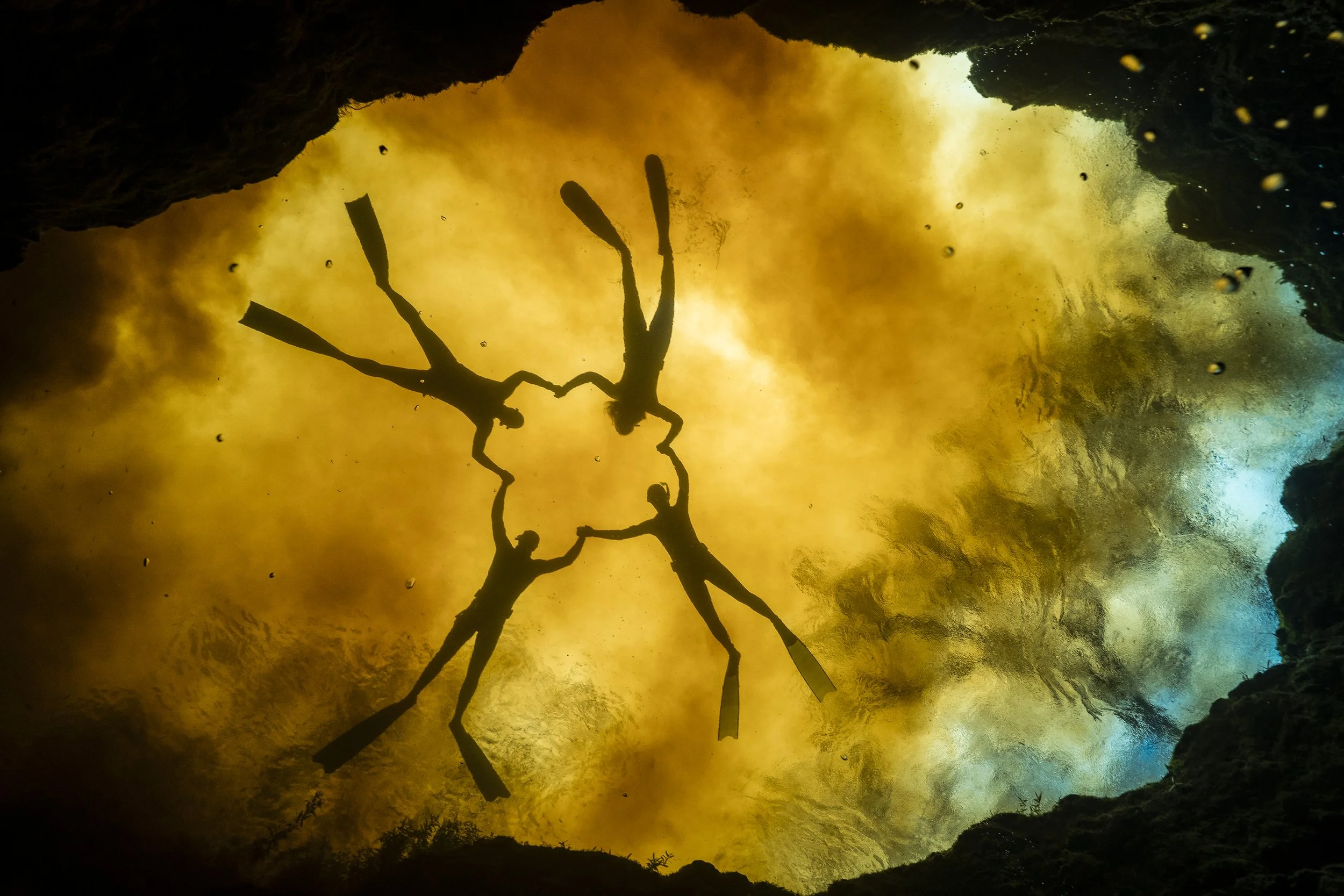 Silhouette of five people holding hands in a circle inside a cave with a glowing, colorful background.
