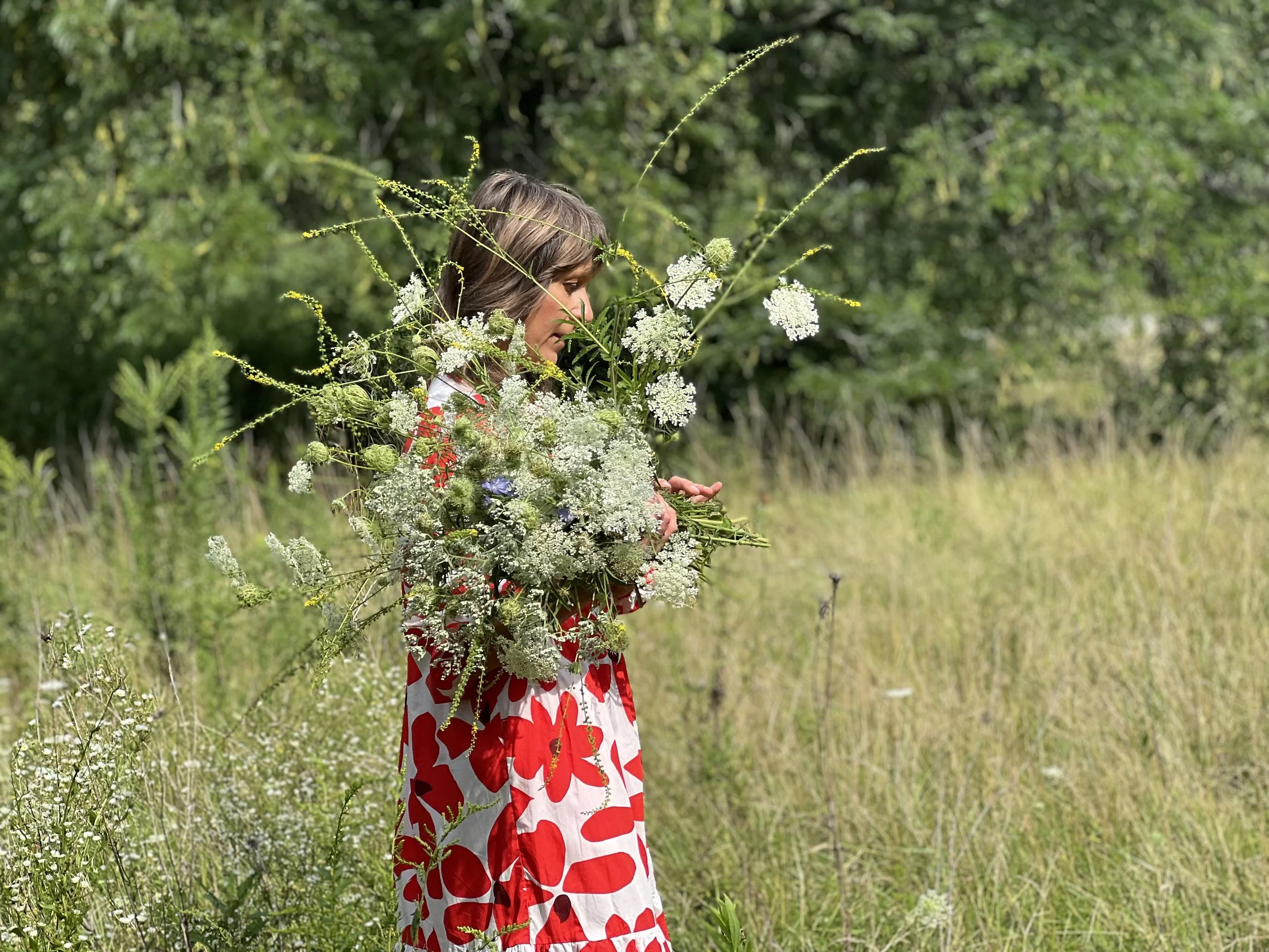 Wilder Bloom founder holding an abundant wildflower-inspired bouquet in a summer meadow.