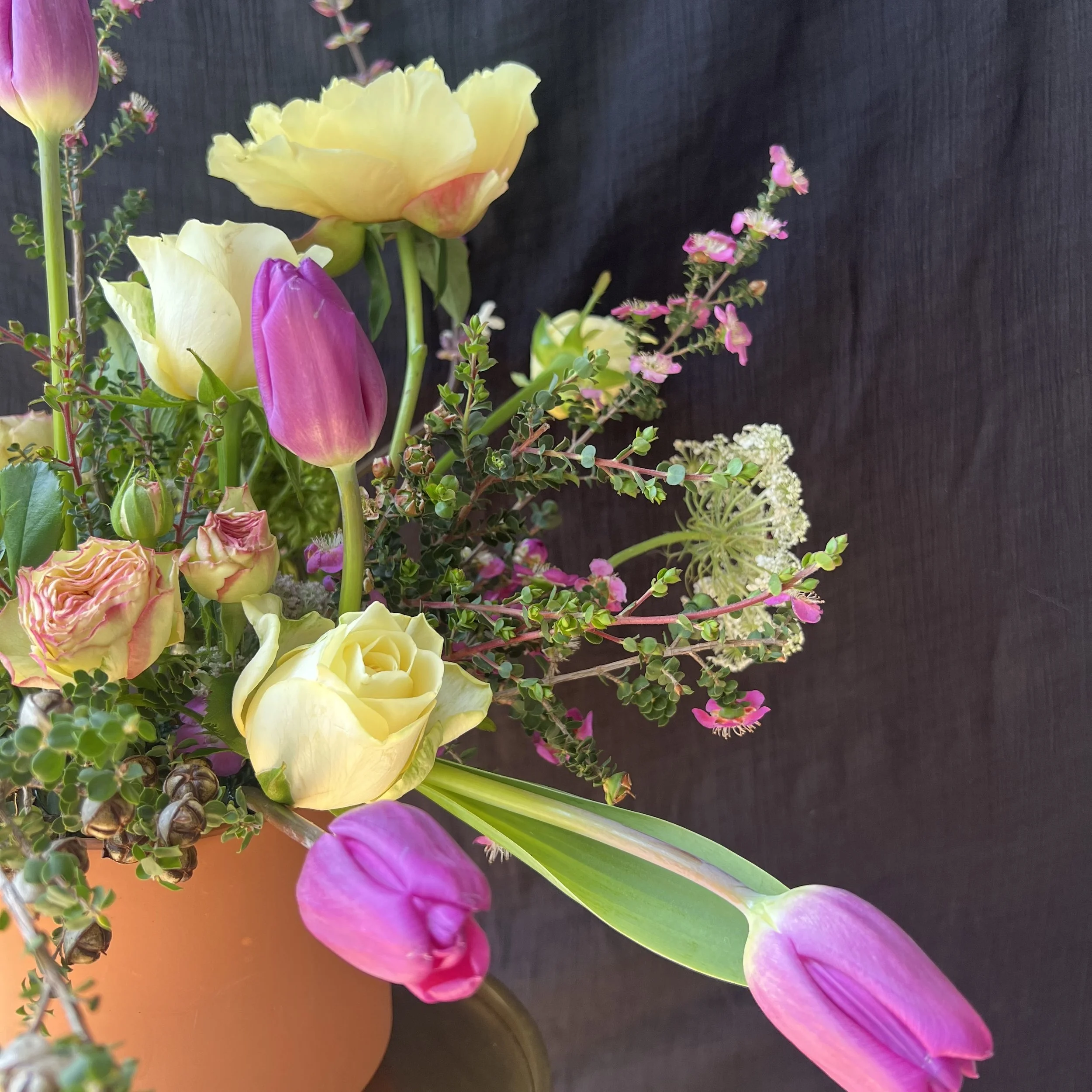 Close-up of tulips, roses, and peonies in vibrant pink and yellow Mother’s Day arrangement