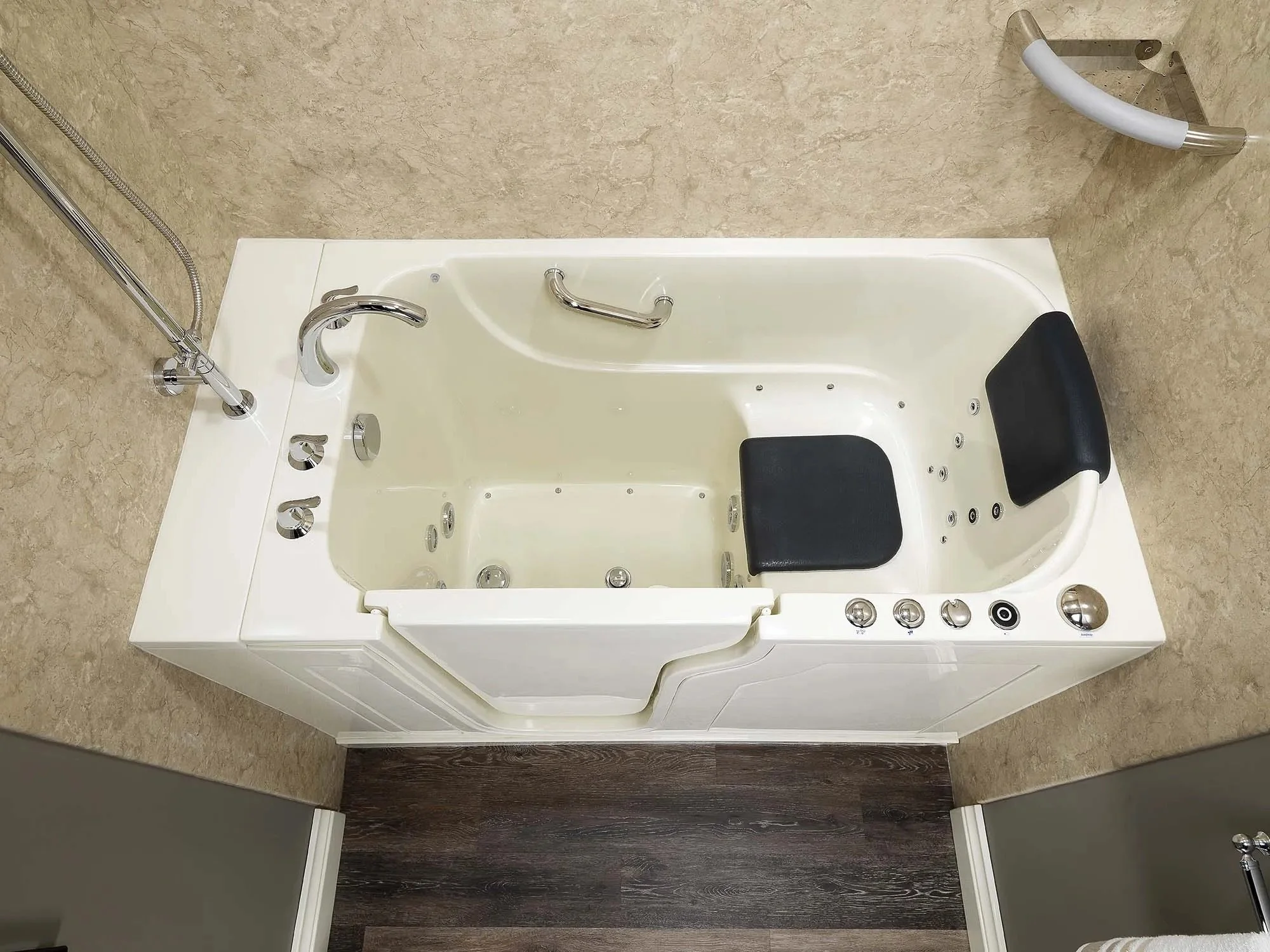 A walk-in bathtub with black cushioned seats, multiple jets, and chrome fixtures in a bathroom with beige walls and dark brown flooring.